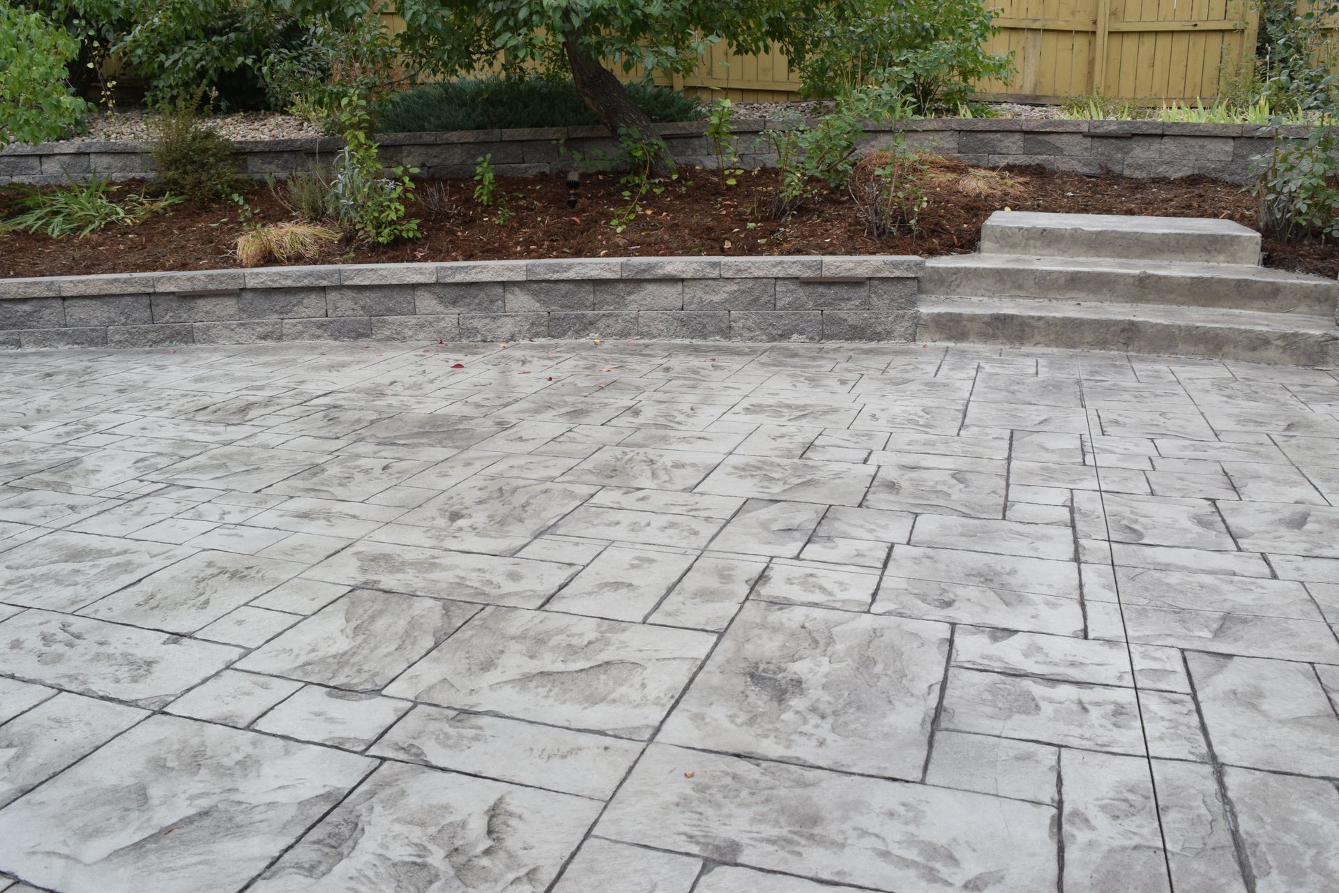 Concrete patio with textured pattern, leading up to a raised garden bed and steps.