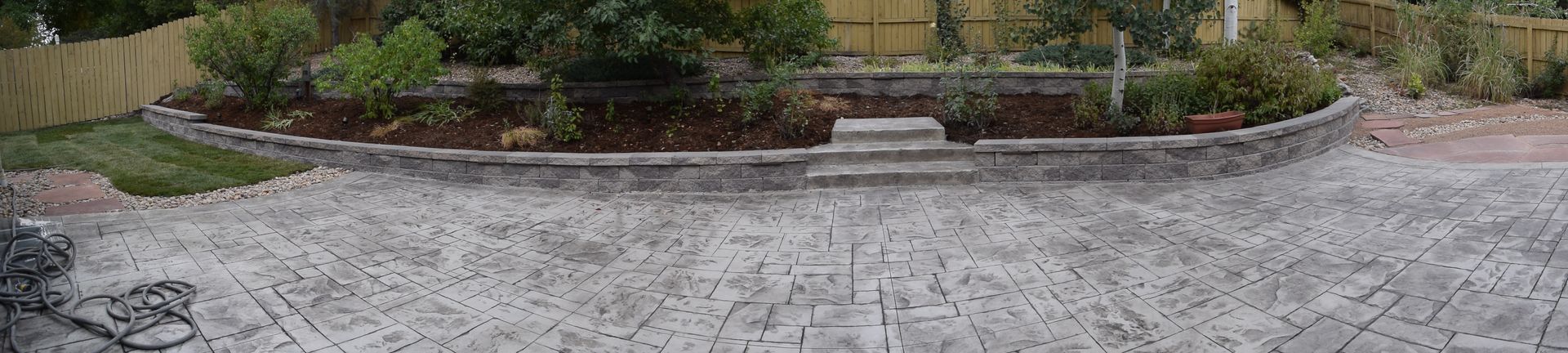 Stone paved driveway leading to a garden bed with plants, bushes, and a small step.