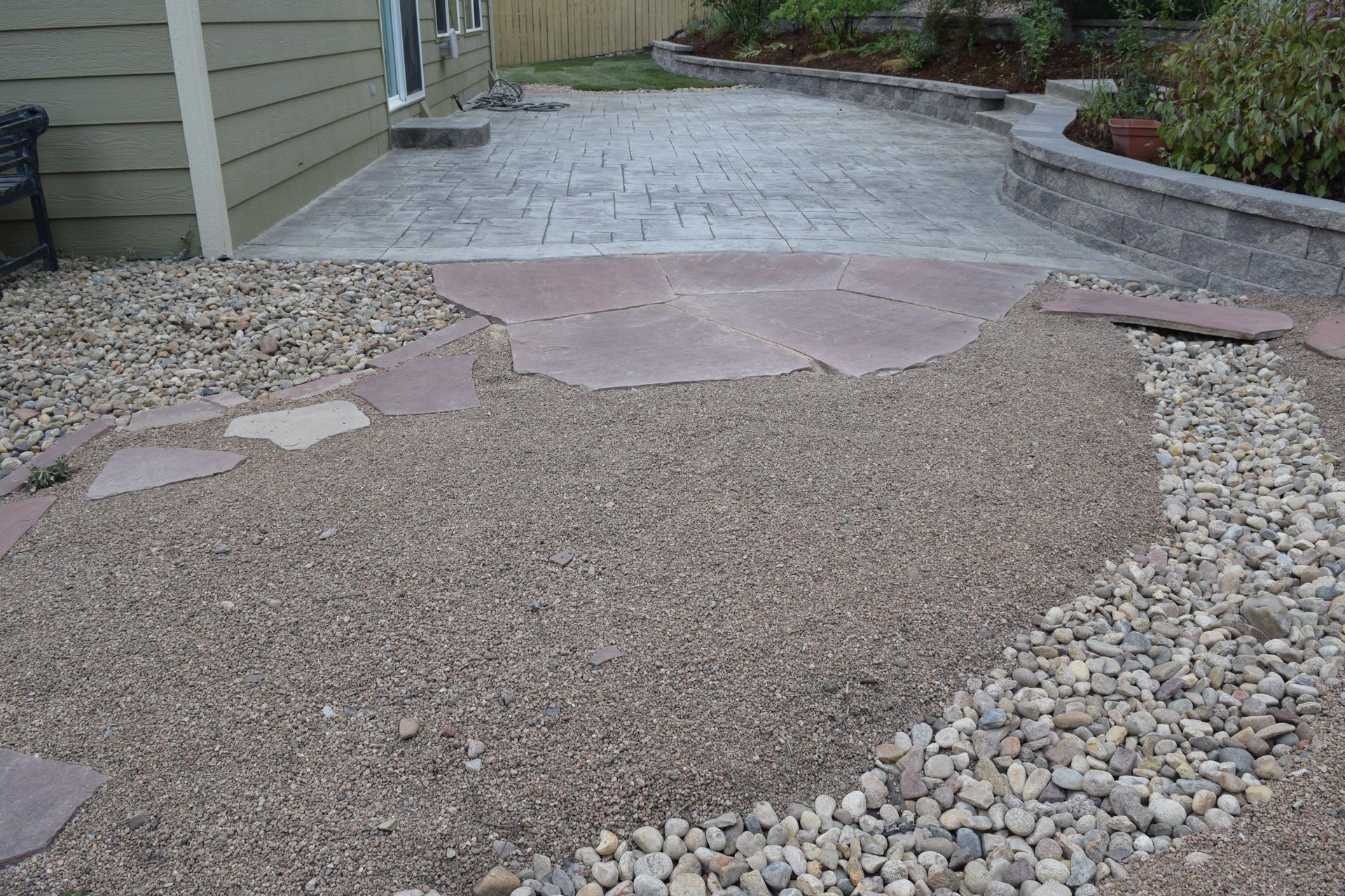 Landscaped yard with gravel, stone pathway leading to patio and retaining wall.