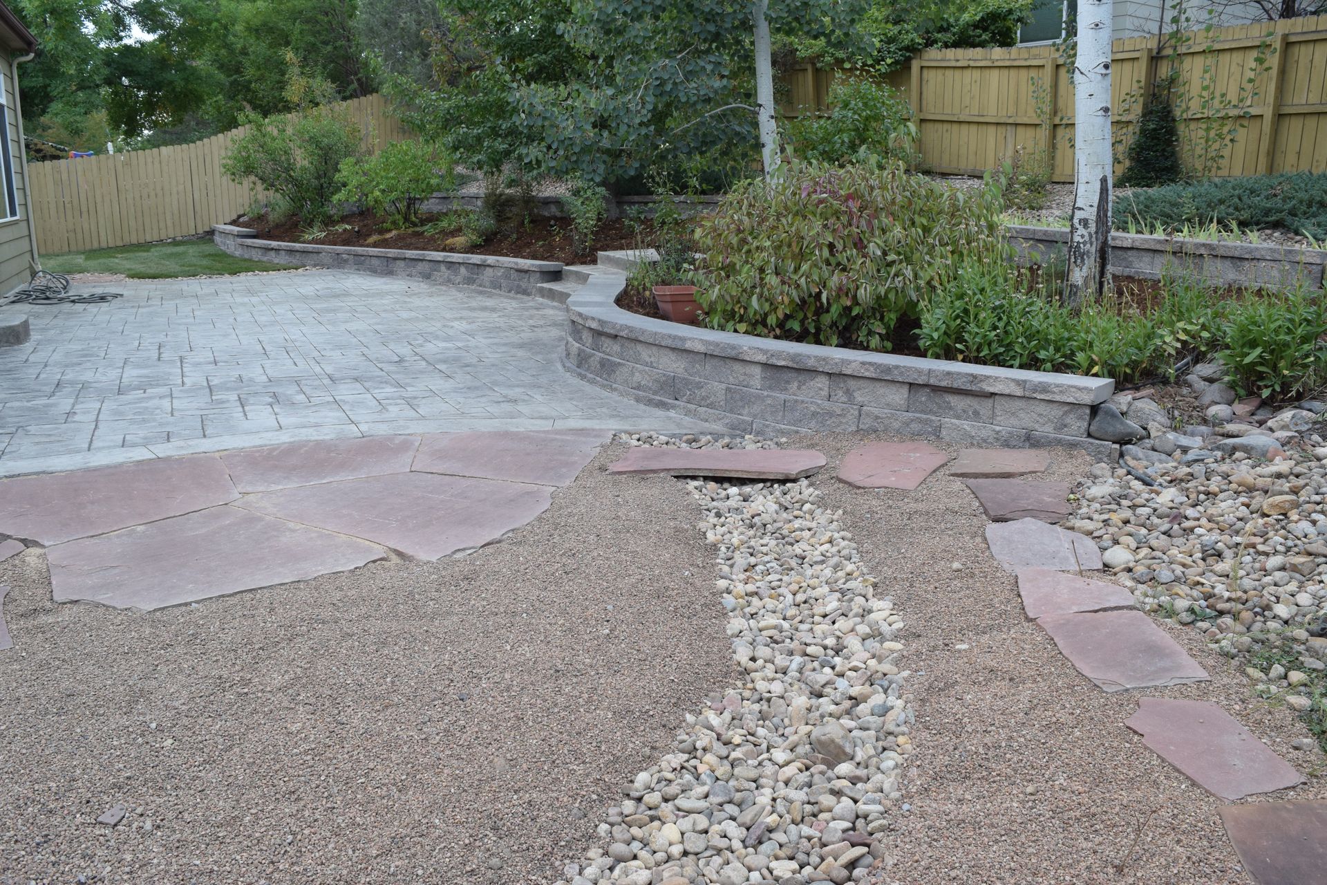Backyard with stamped concrete patio, rock garden, retaining wall, and landscaping.