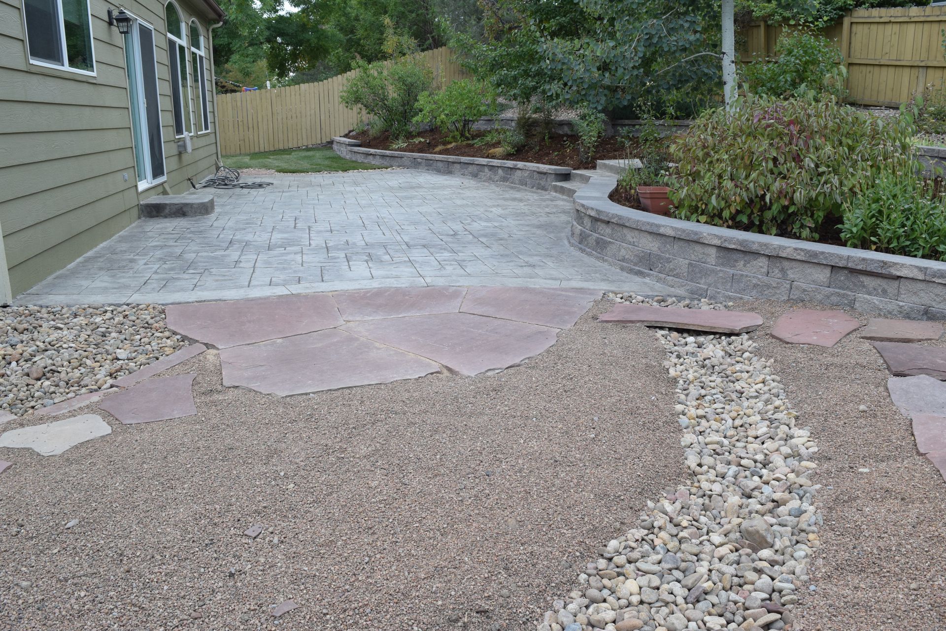 Backyard patio with stamped concrete, gravel path, and retaining wall.