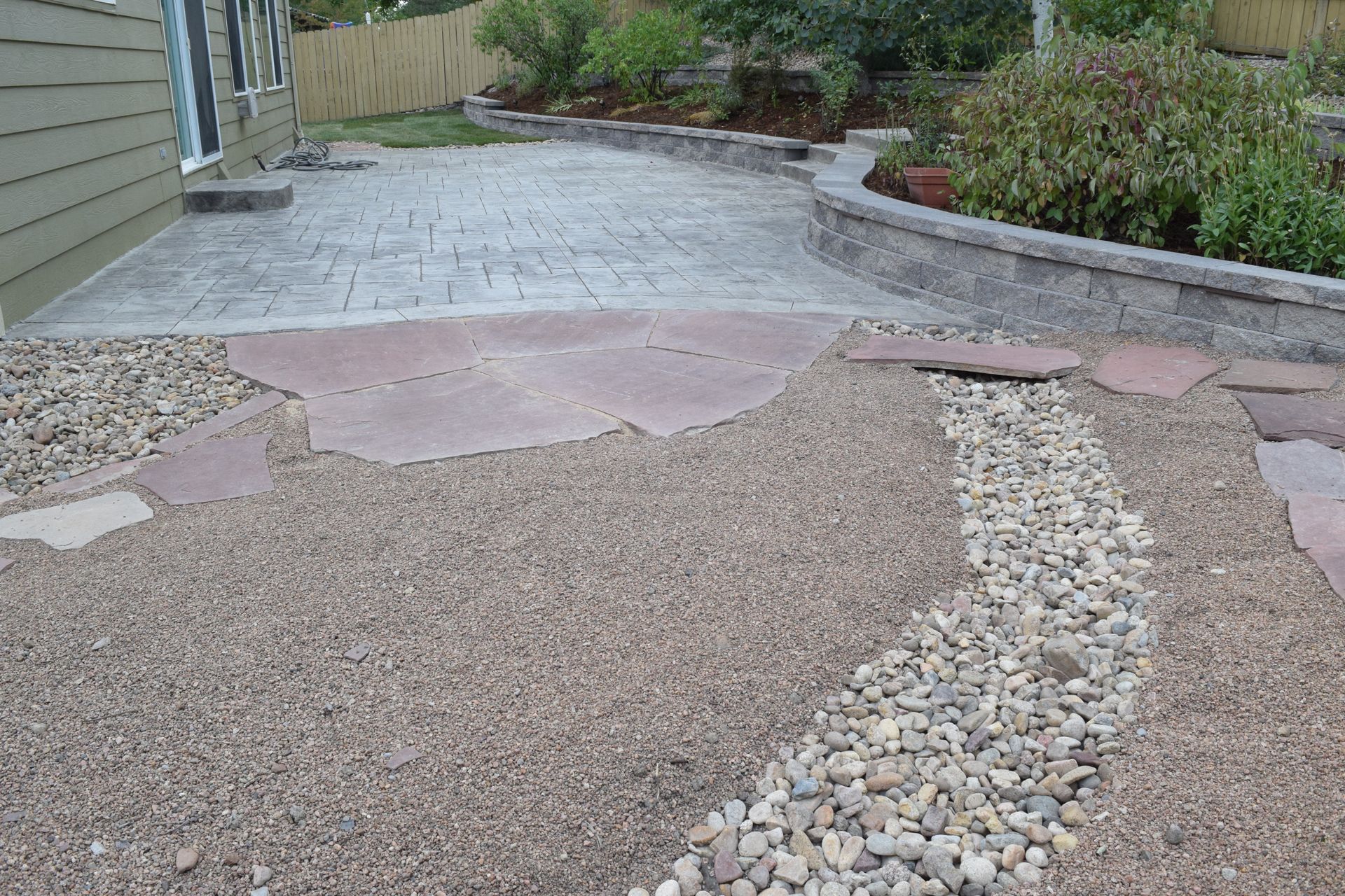 Backyard patio with gravel, stepping stones, and a small rock 