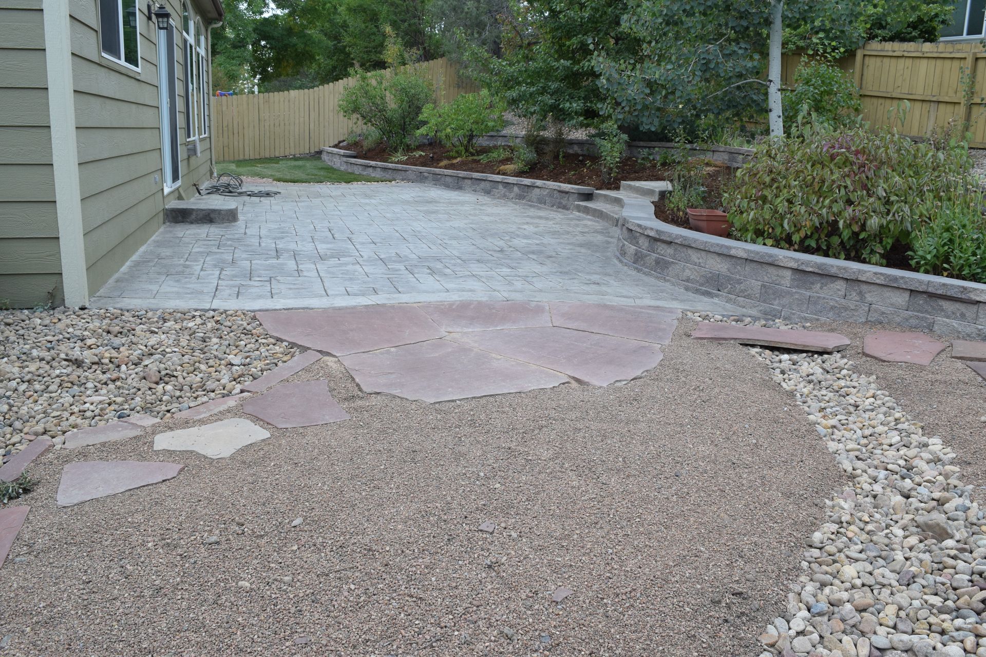 Backyard patio with gravel, flagstones, and a retaining wall.