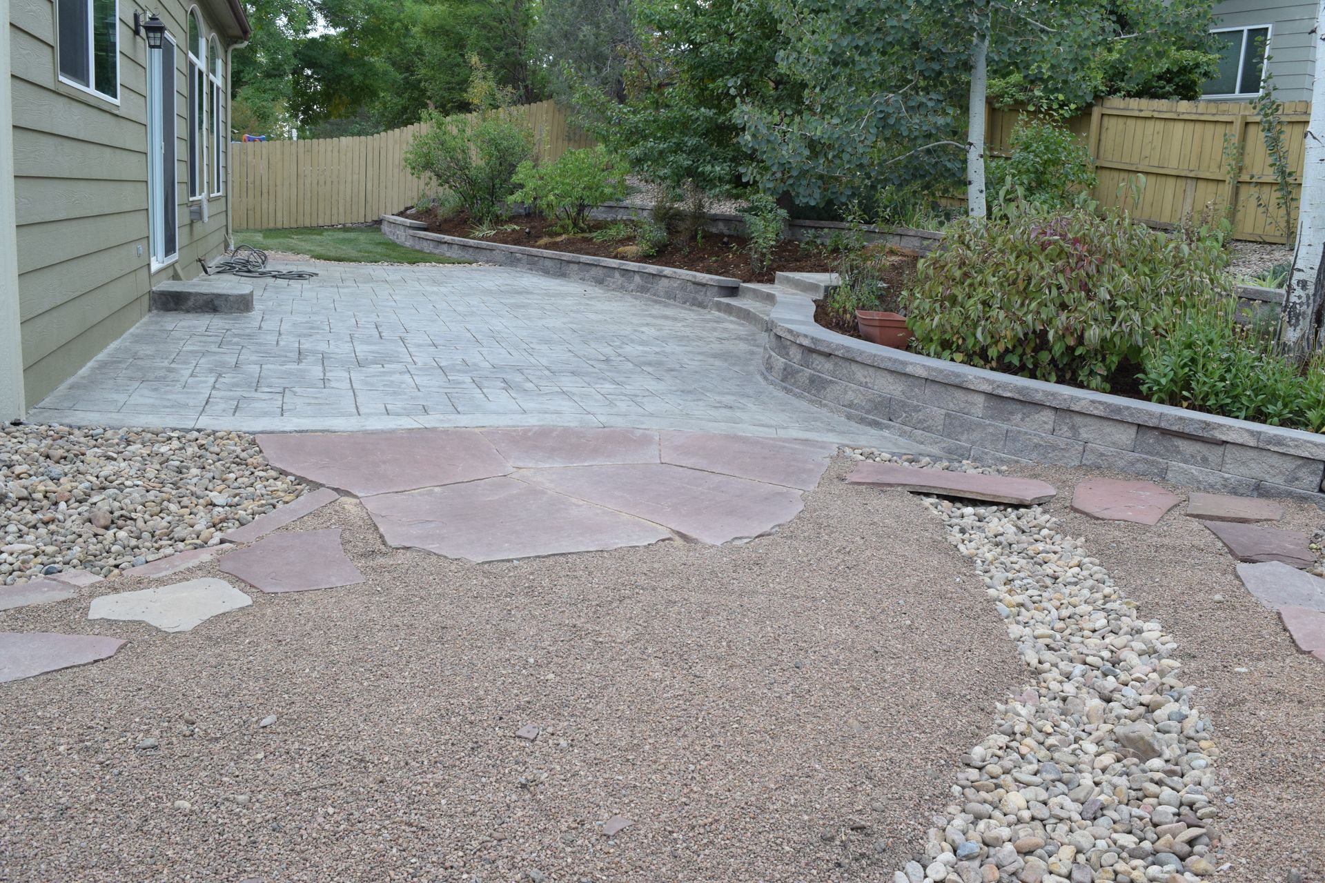 Backyard patio with gravel, stone pavers, and retaining wall.