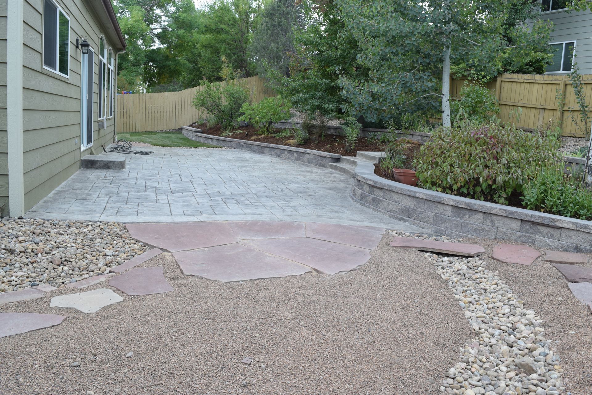Backyard with stone patio, retaining wall, and landscaping.