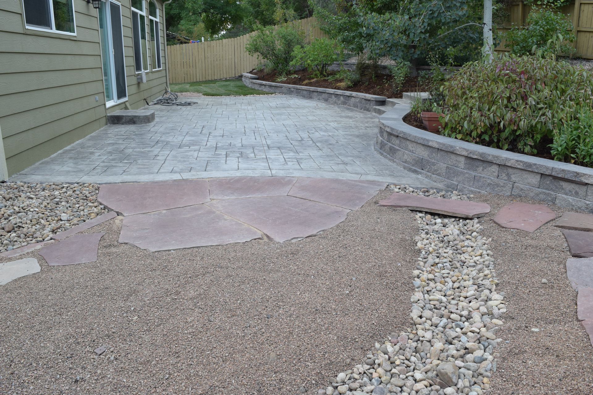 A backyard patio with stamped concrete and stone path leading to a raised garden bed.