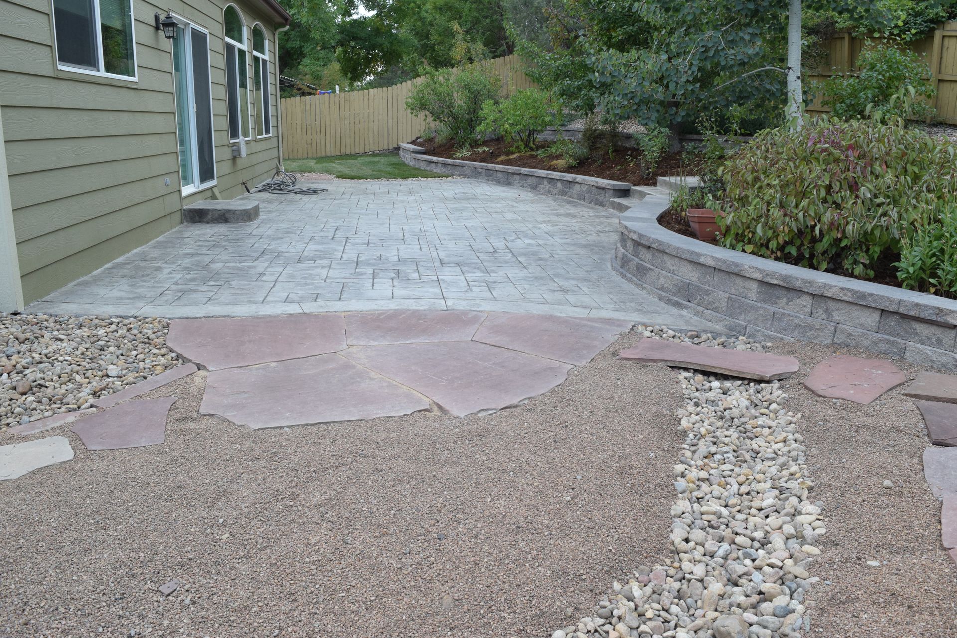 Backyard patio with stamped concrete, rock pathway, and retaining wall.