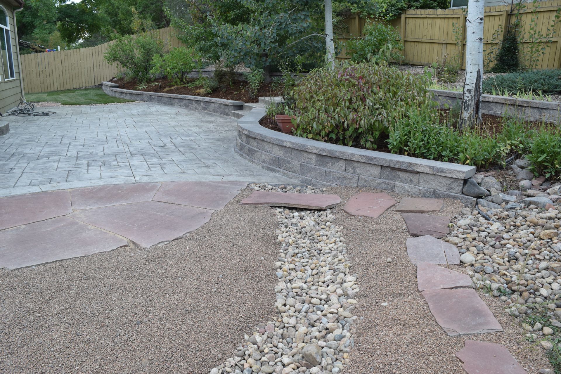 Patio with textured pavers, gravel pathway, retaining wall, and landscaping.