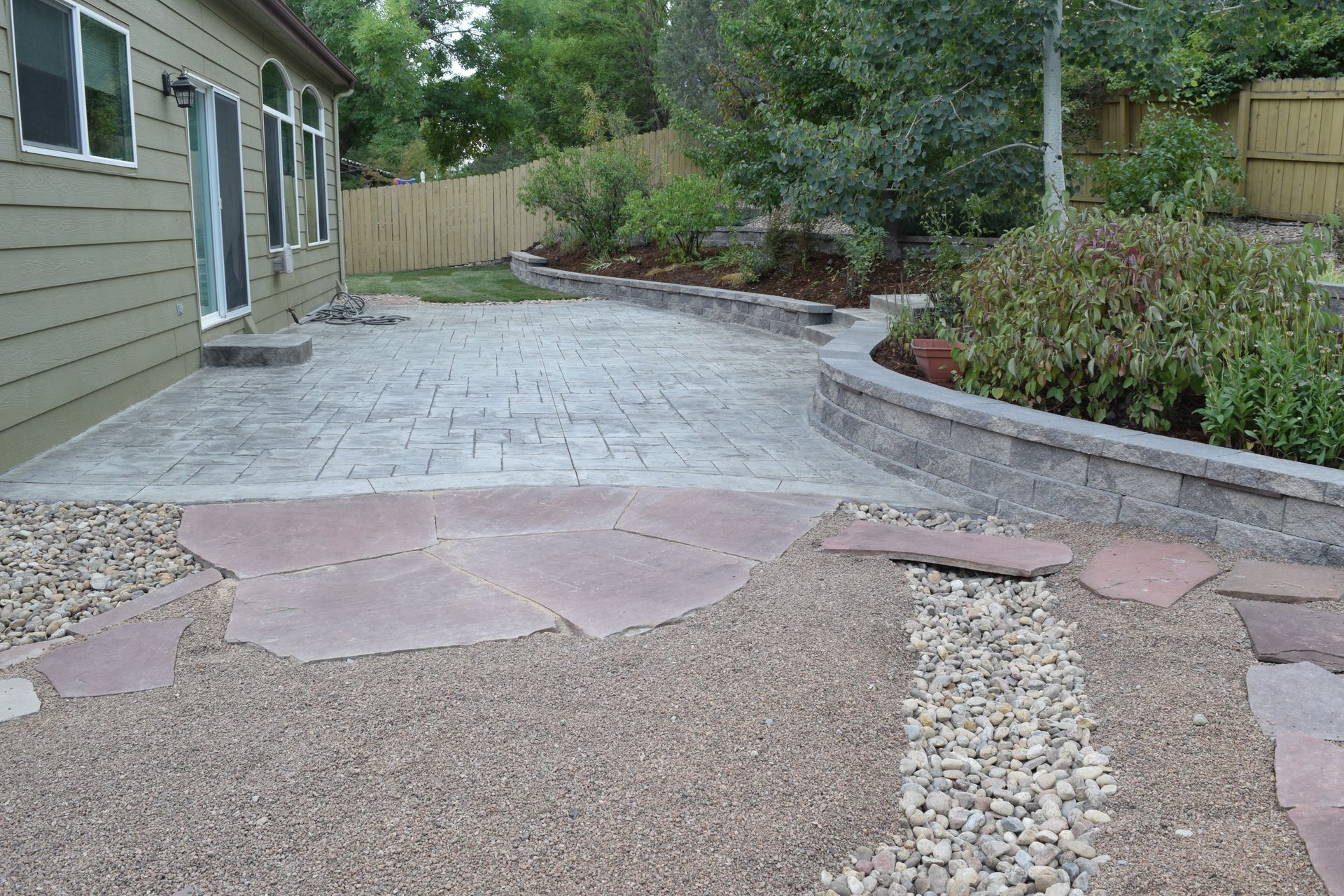 Backyard patio with stamped concrete, gravel paths, and a retaining wall.