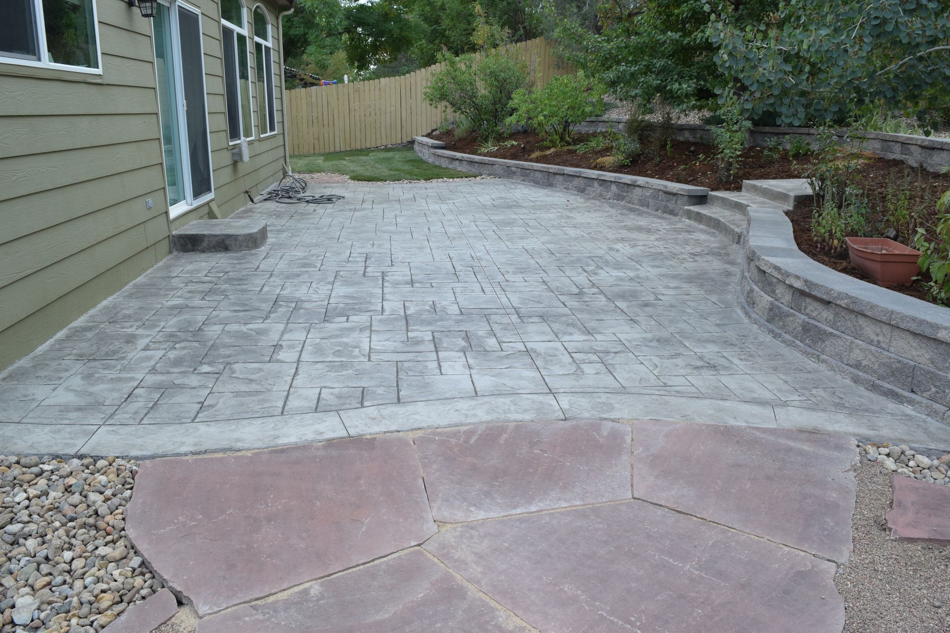 Concrete patio with a pathway and retaining wall in a backyard setting.