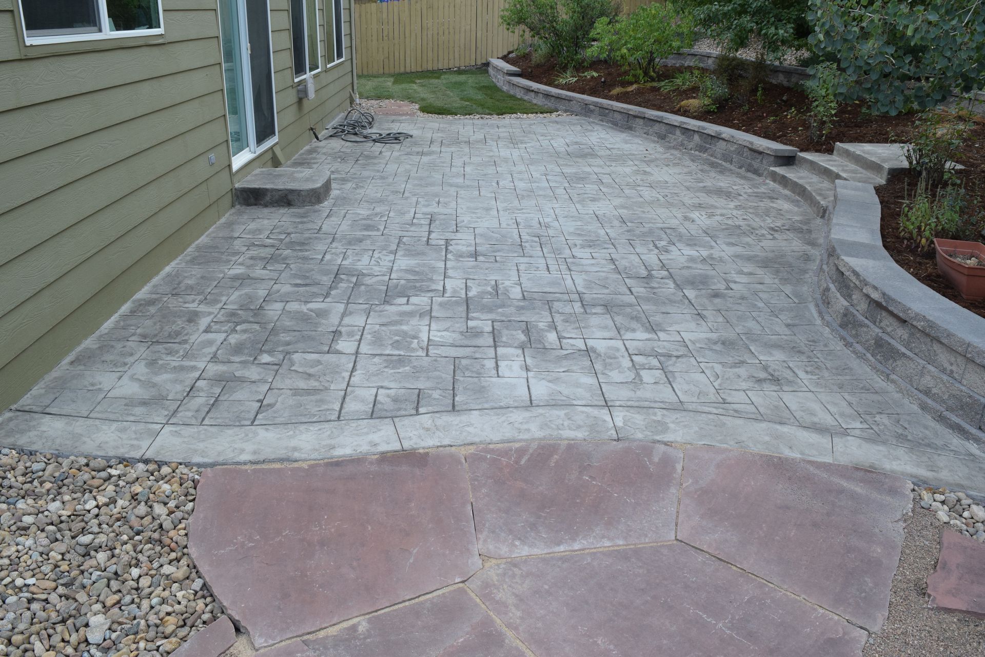 Gray stamped concrete patio with stone path and retaining wall.