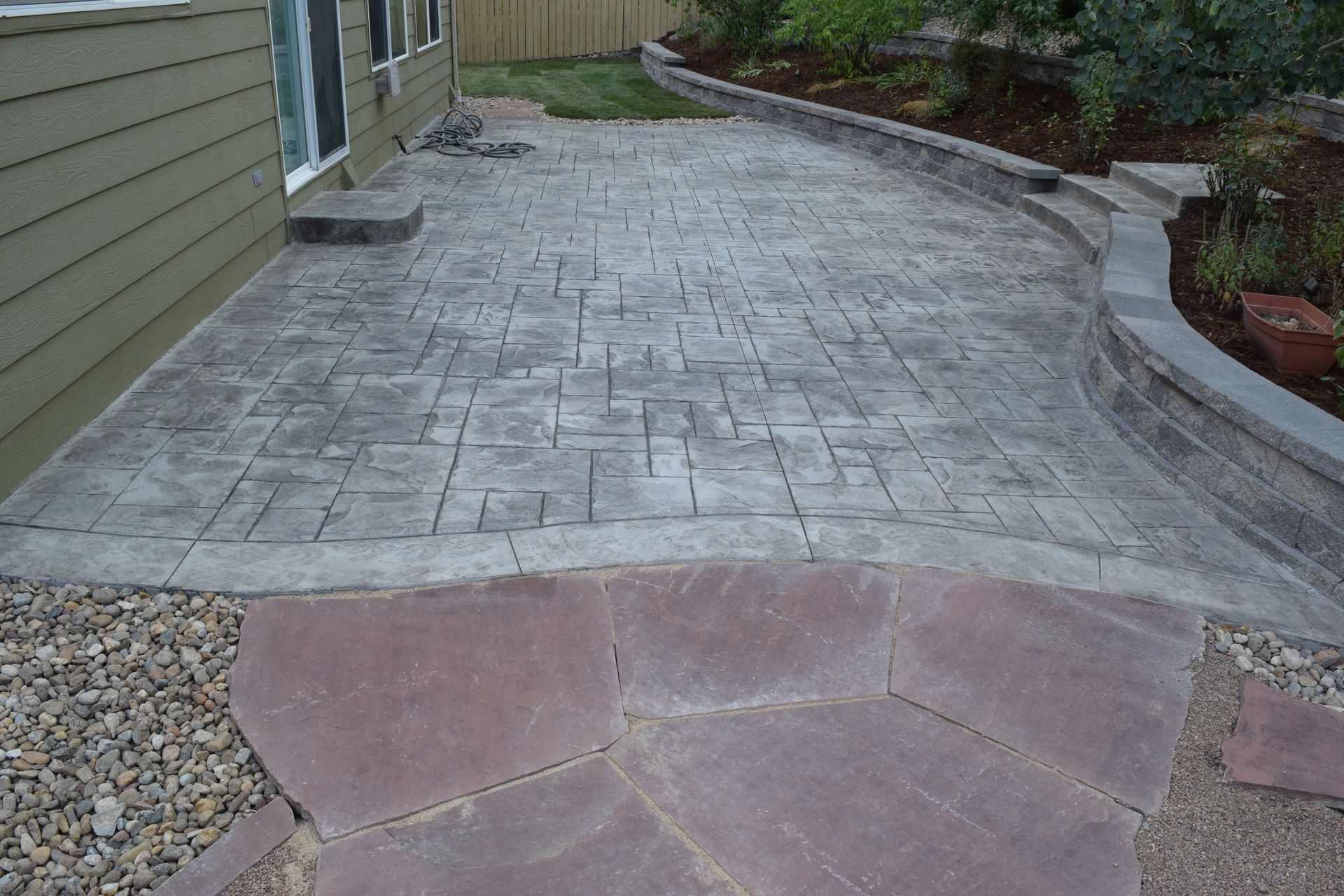 Patio with patterned gray concrete, reddish stone path, and retaining wall.