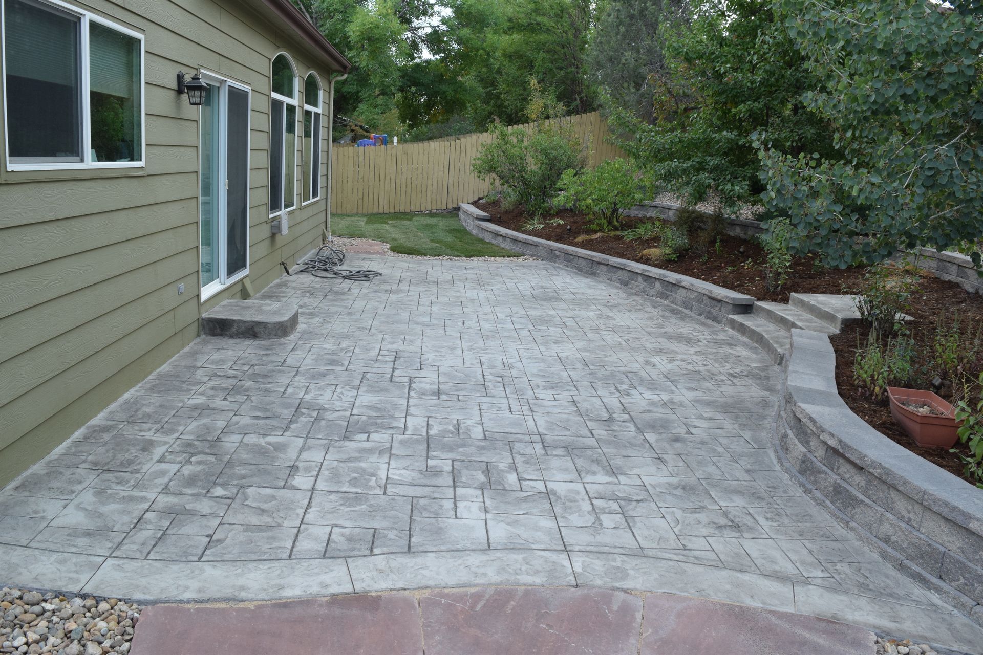 Patio with textured concrete, low retaining wall, and backyard landscaping.
