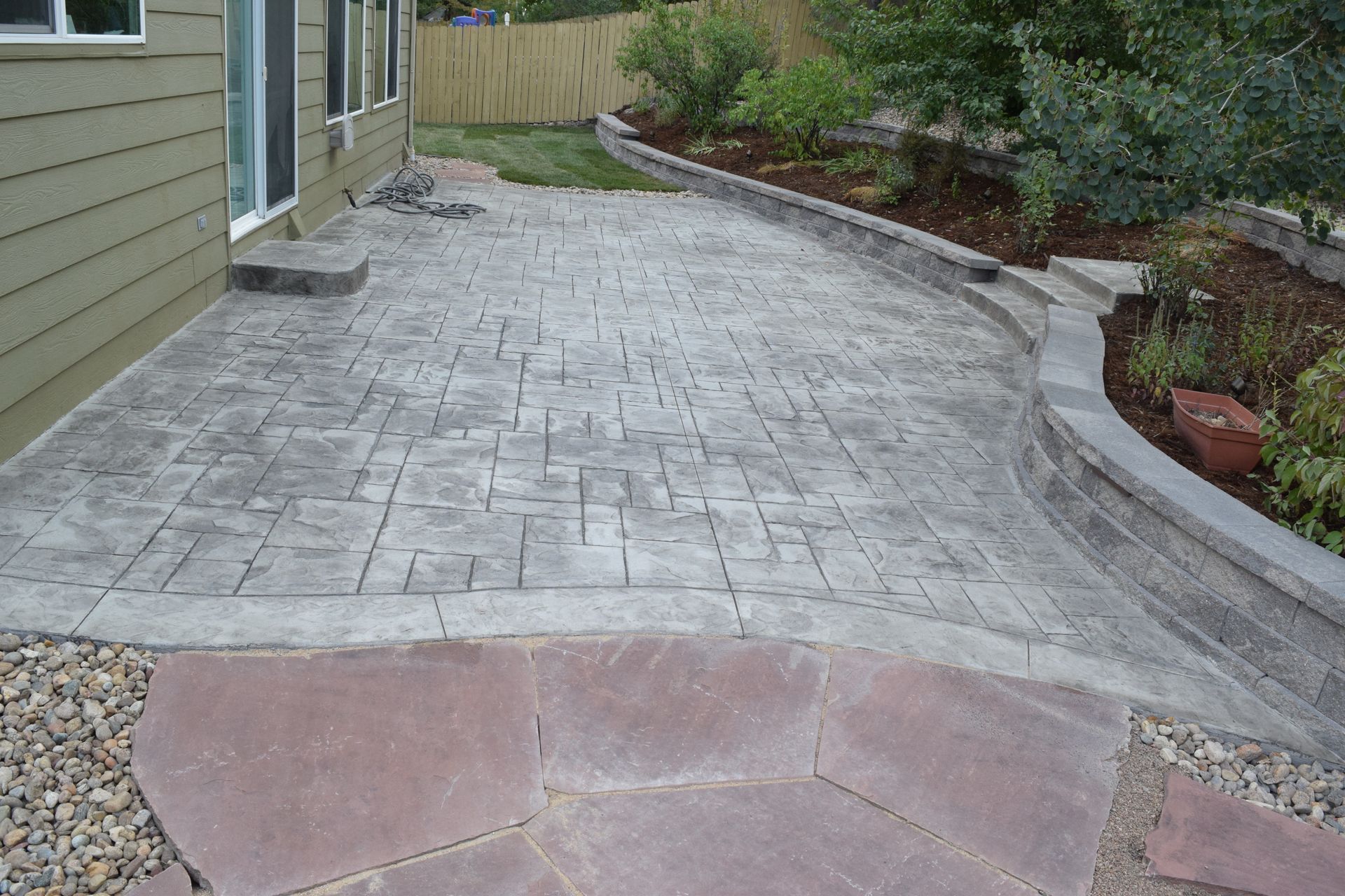 Concrete patio with textured surface, pathway, retaining wall, and backyard.