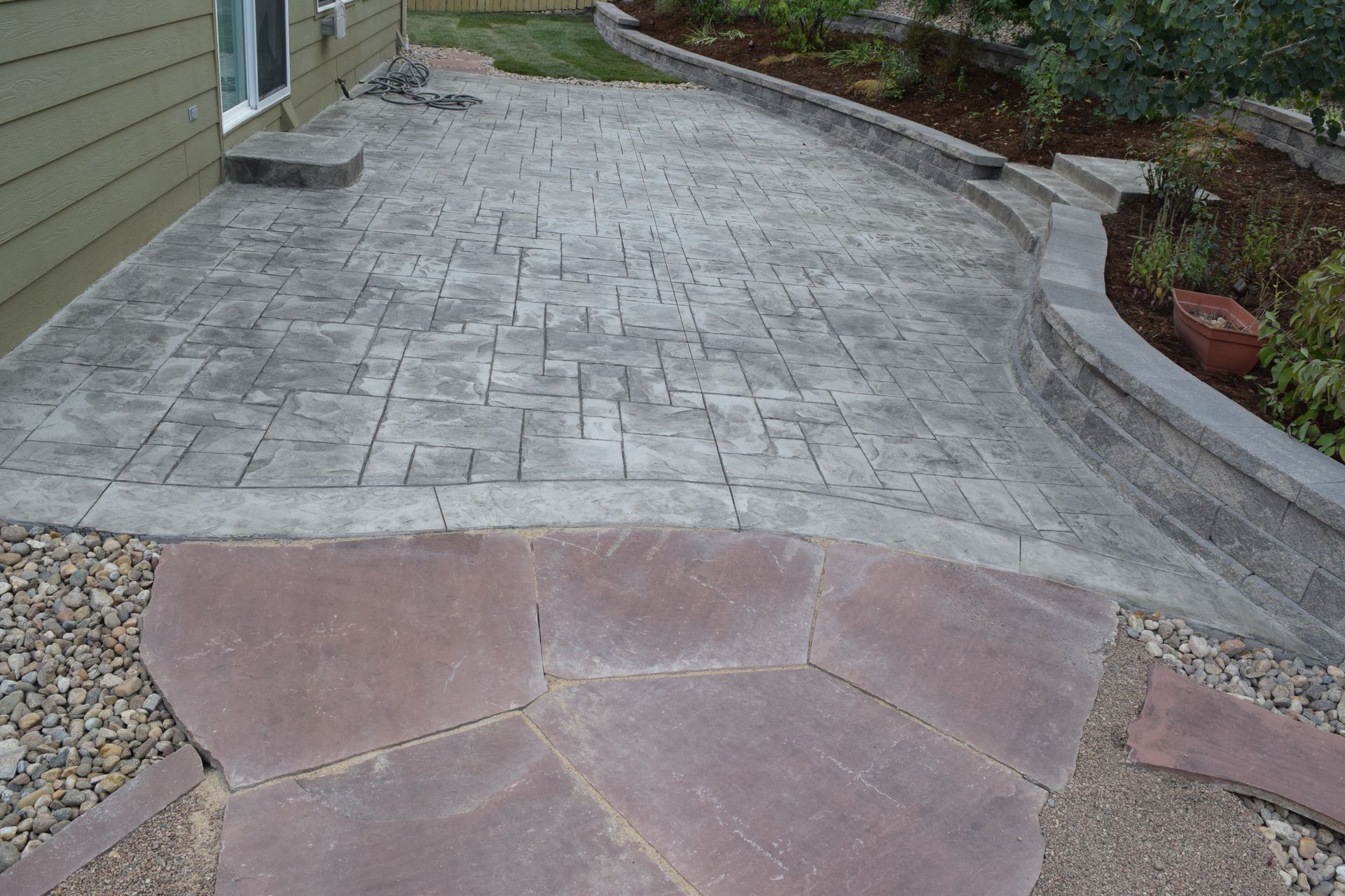 Stamped concrete patio with a stone pathway and retaining wall.