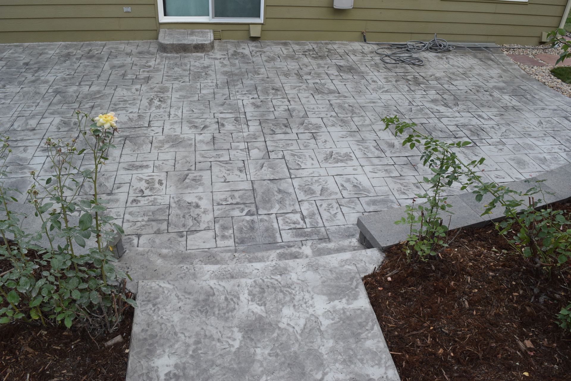 Stamped concrete patio with steps and small flower bushes.
