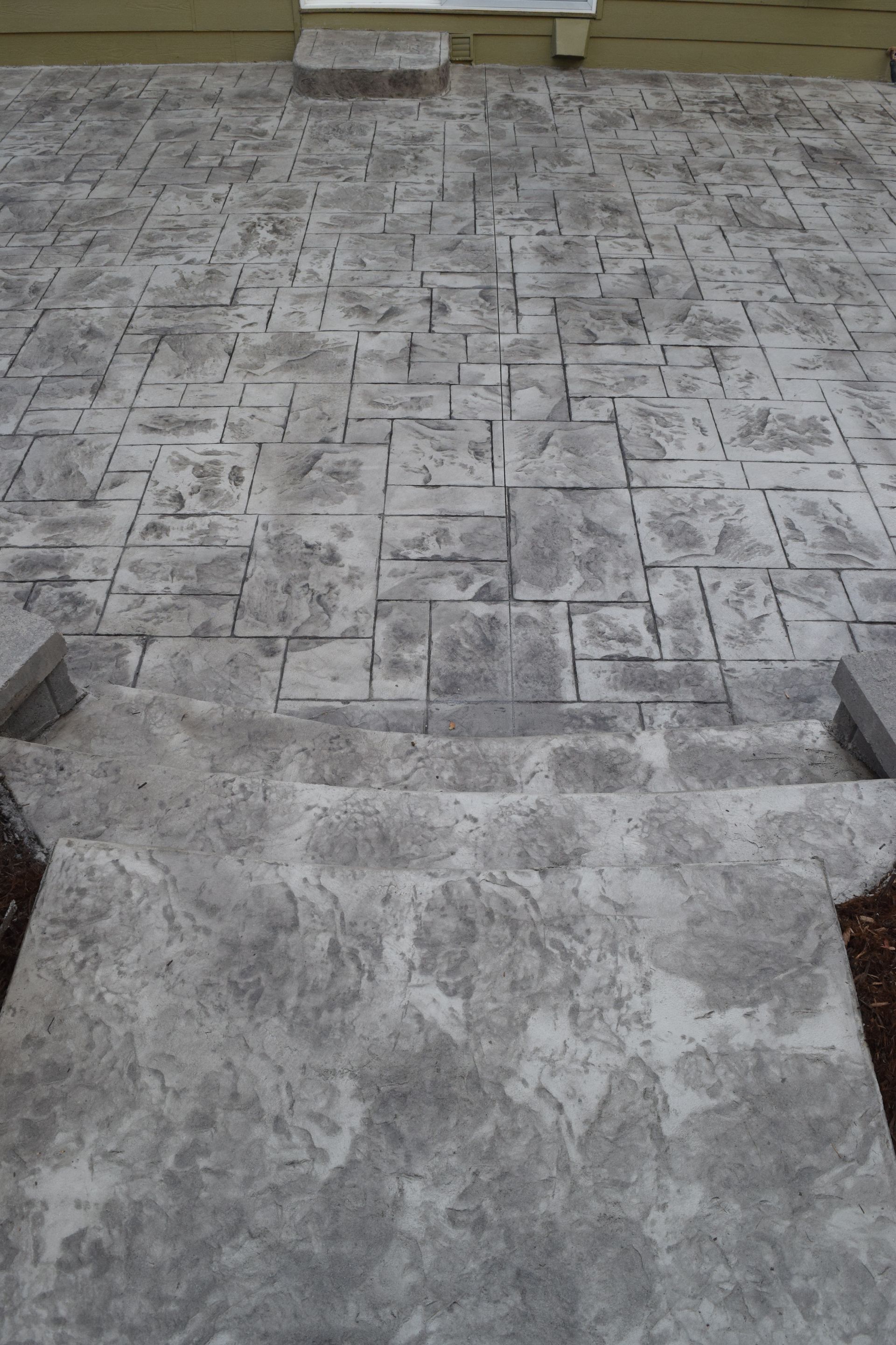 Gray concrete patio with block and stone patterns, near a building.