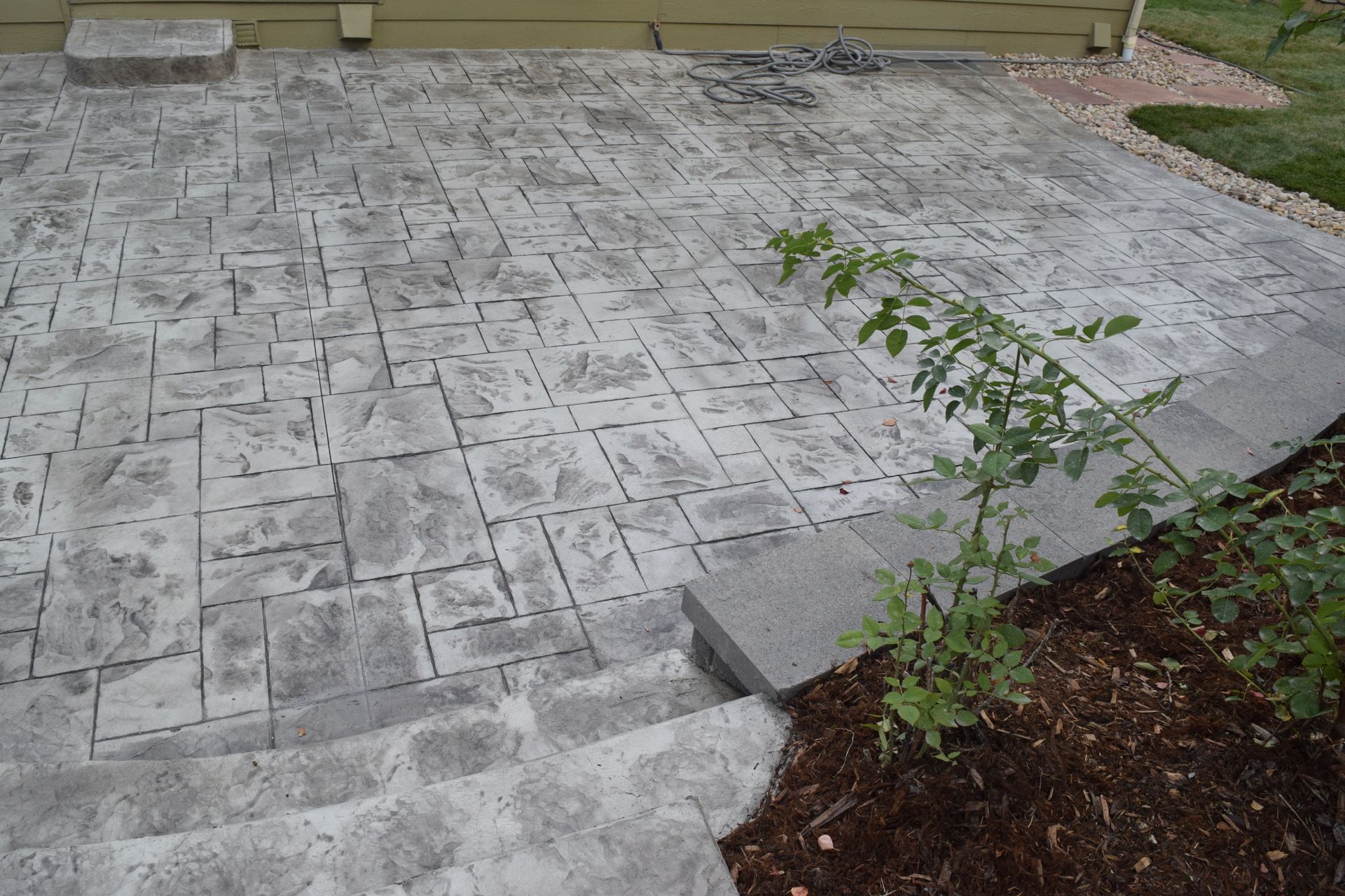 Concrete patio with patterned surface, stepping down into a landscaped area with mulch and green plants.