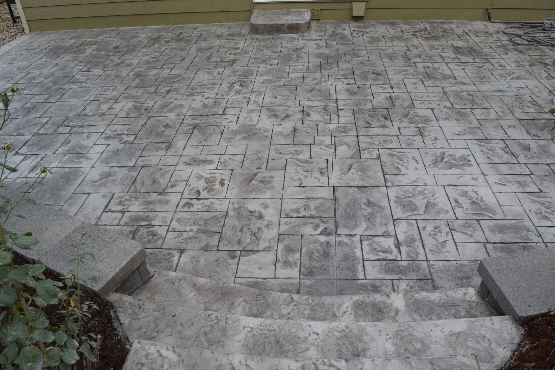 Concrete patio with patterned stone design, steps, and two small retaining walls.