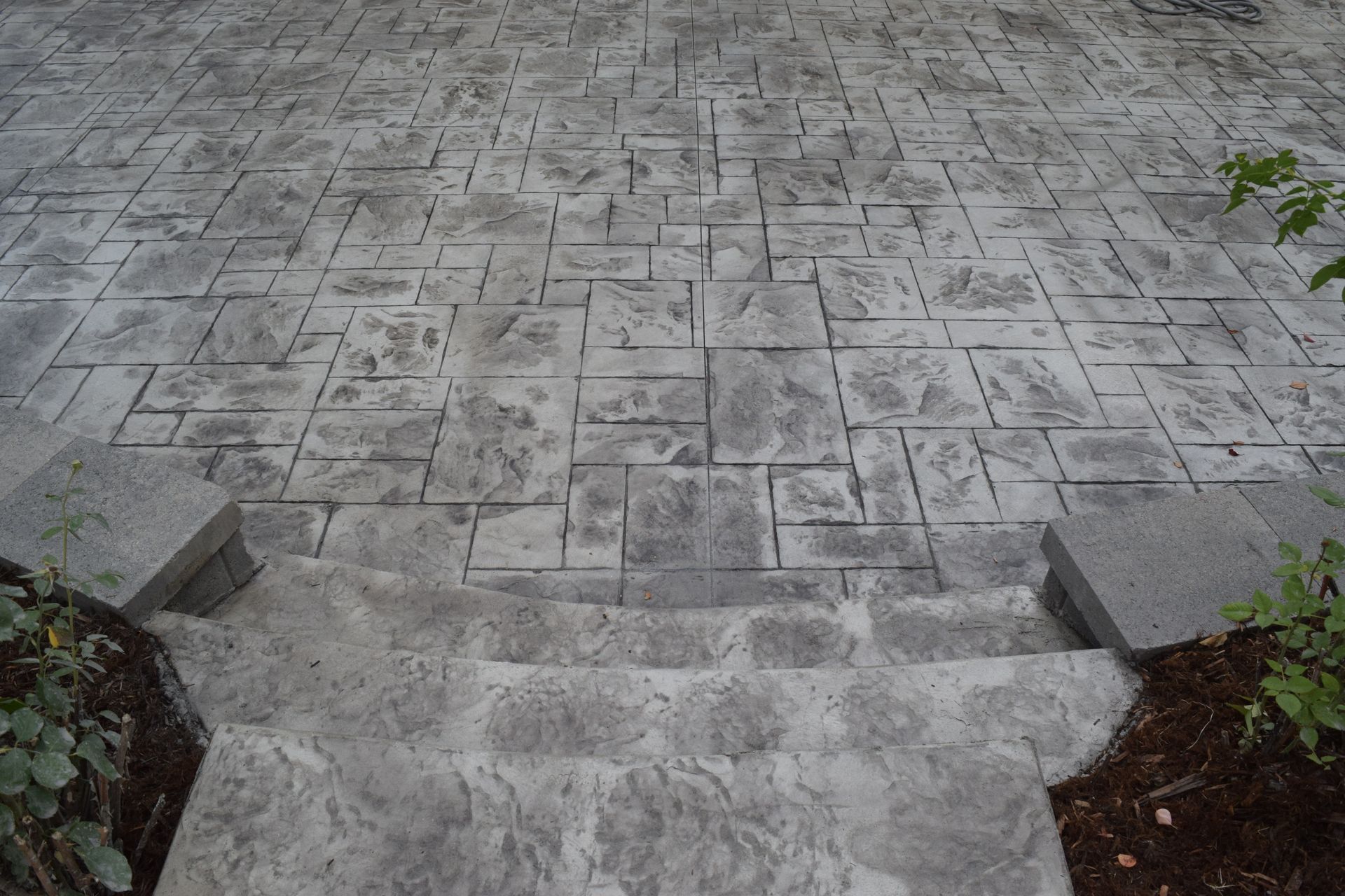 Gray concrete patio with steps leading down, textured with a rectangular pattern.