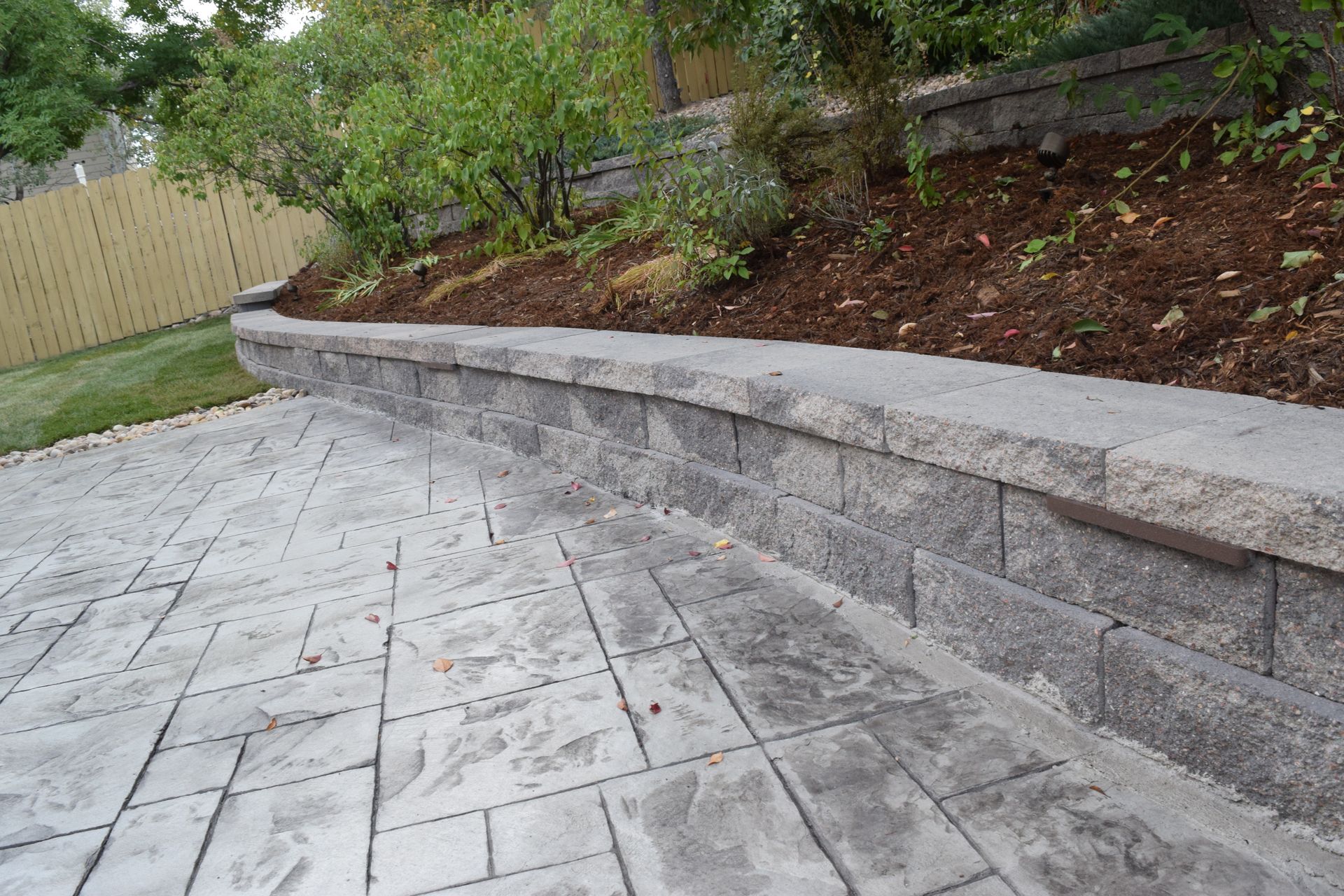 Stone retaining wall separating a patio and a hillside garden.
