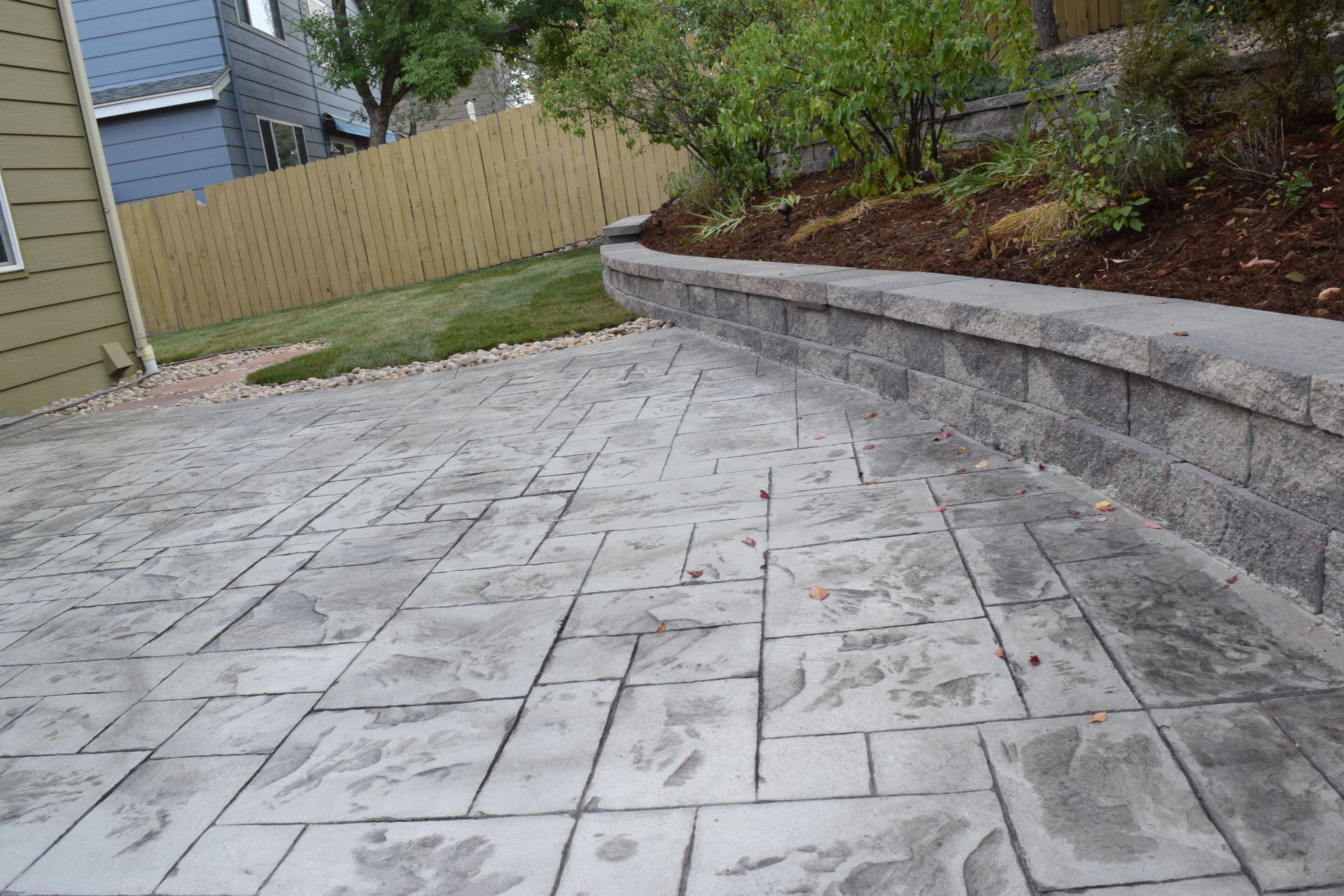 Stamped concrete patio with a retaining wall and grass against a wooden fence.