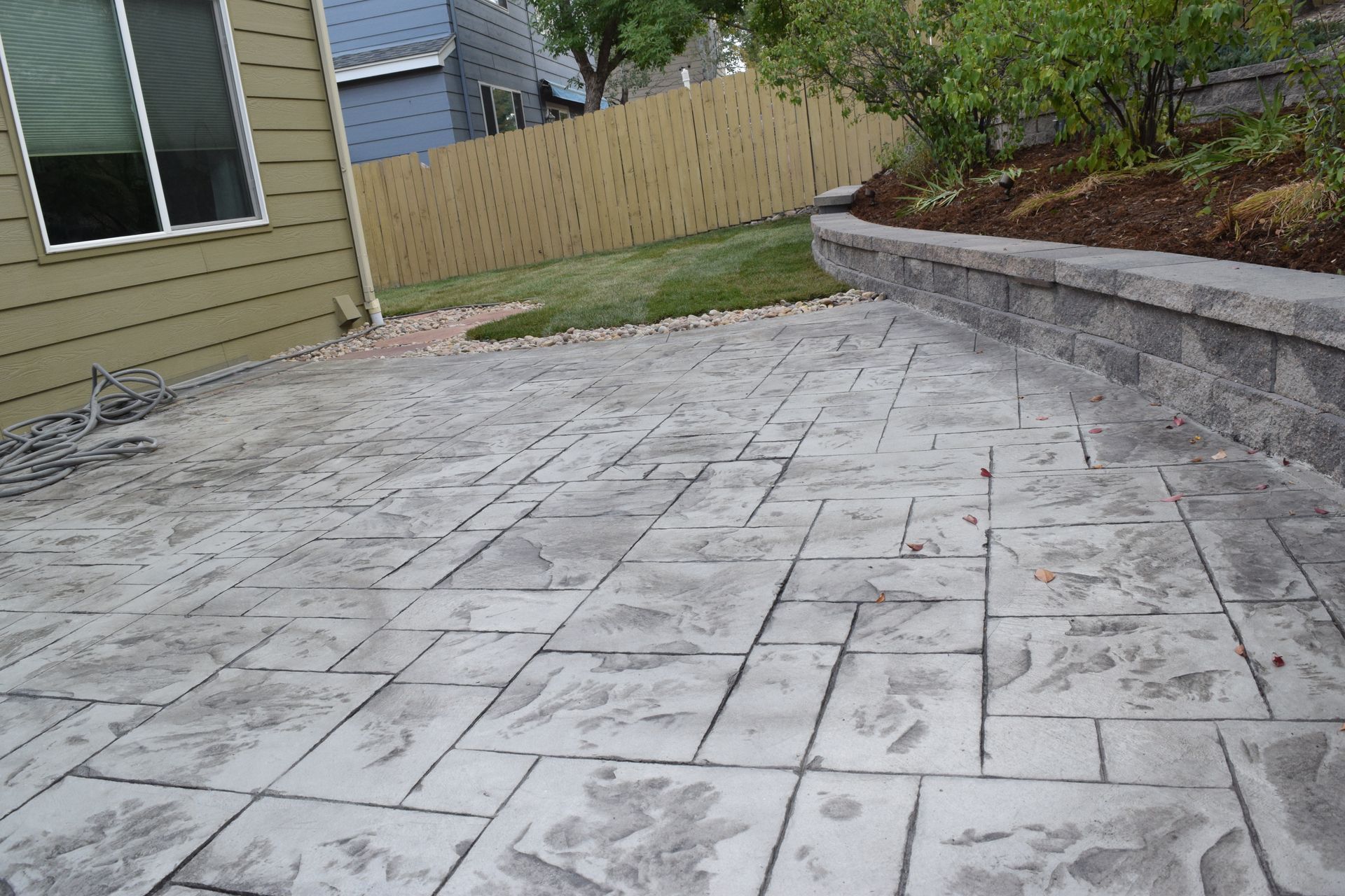 Stamped concrete patio in backyard next to retaining wall and lawn.