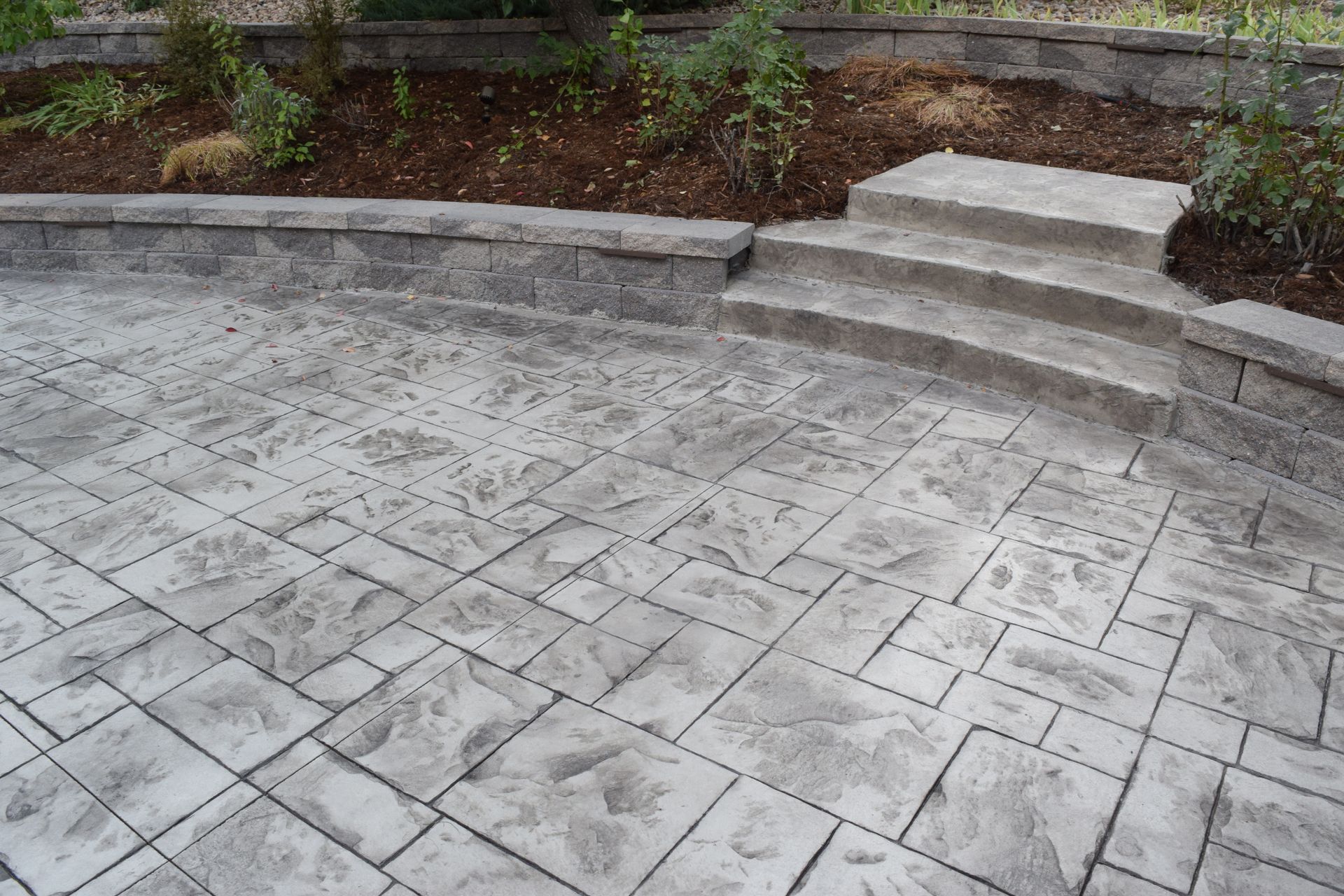 Stamped concrete patio with steps leading to a raised garden bed. Gray tones.