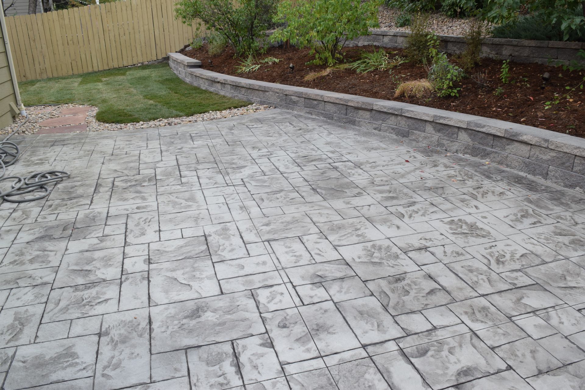 Stamped concrete patio with a retaining wall, a small lawn, and wooden fence.