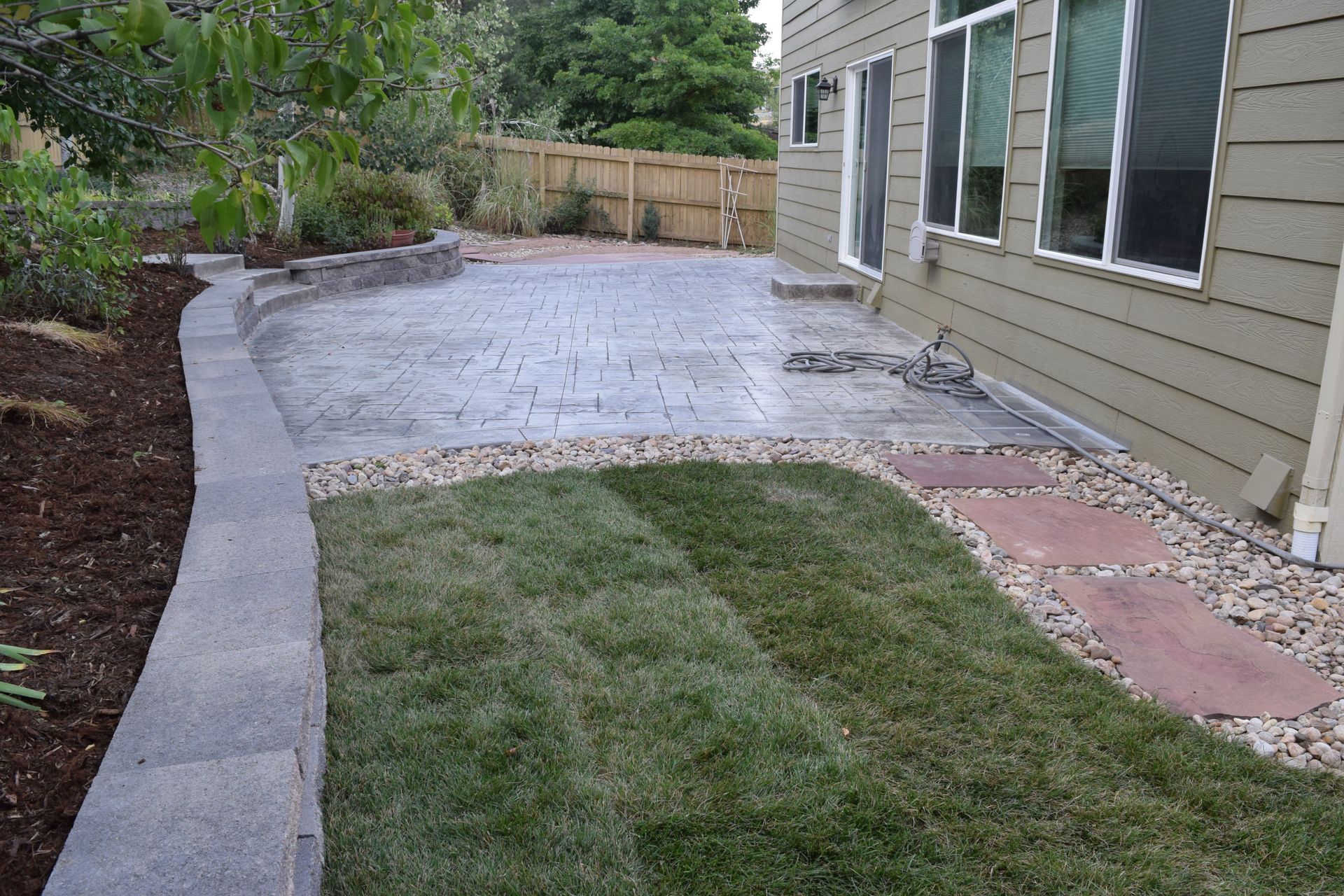 Patio and lawn next to a house with a concrete border, mulched flowerbed, and rock edging.
