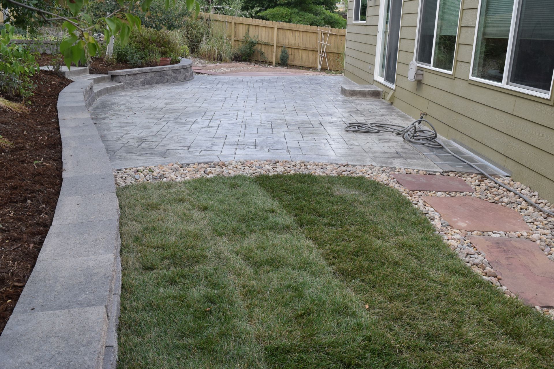 Backyard patio with gray pavers, grass, stone border, and house.