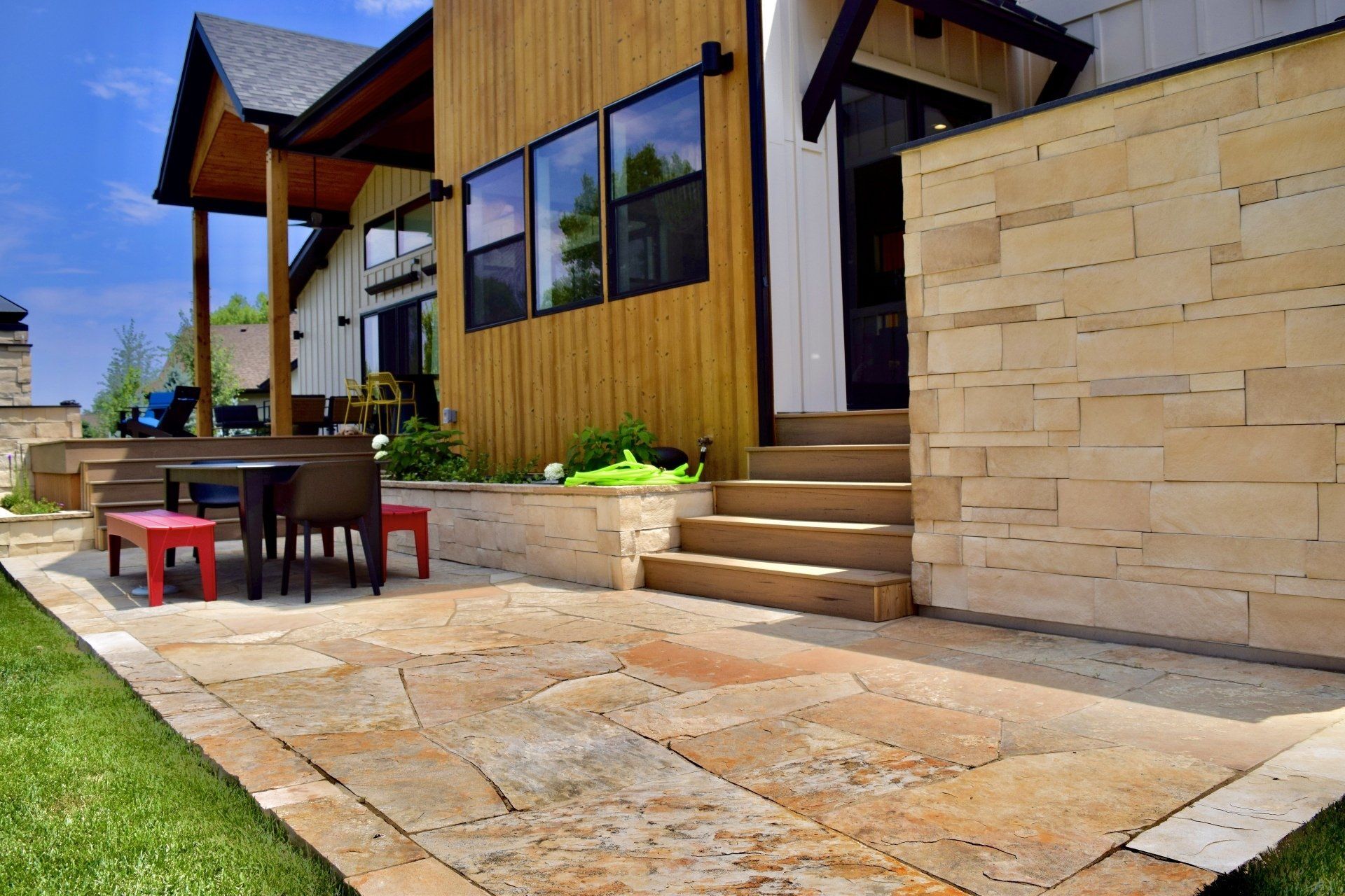 Patio with stone pavers, wooden siding, and a stone retaining wall, with a small table and red benches.