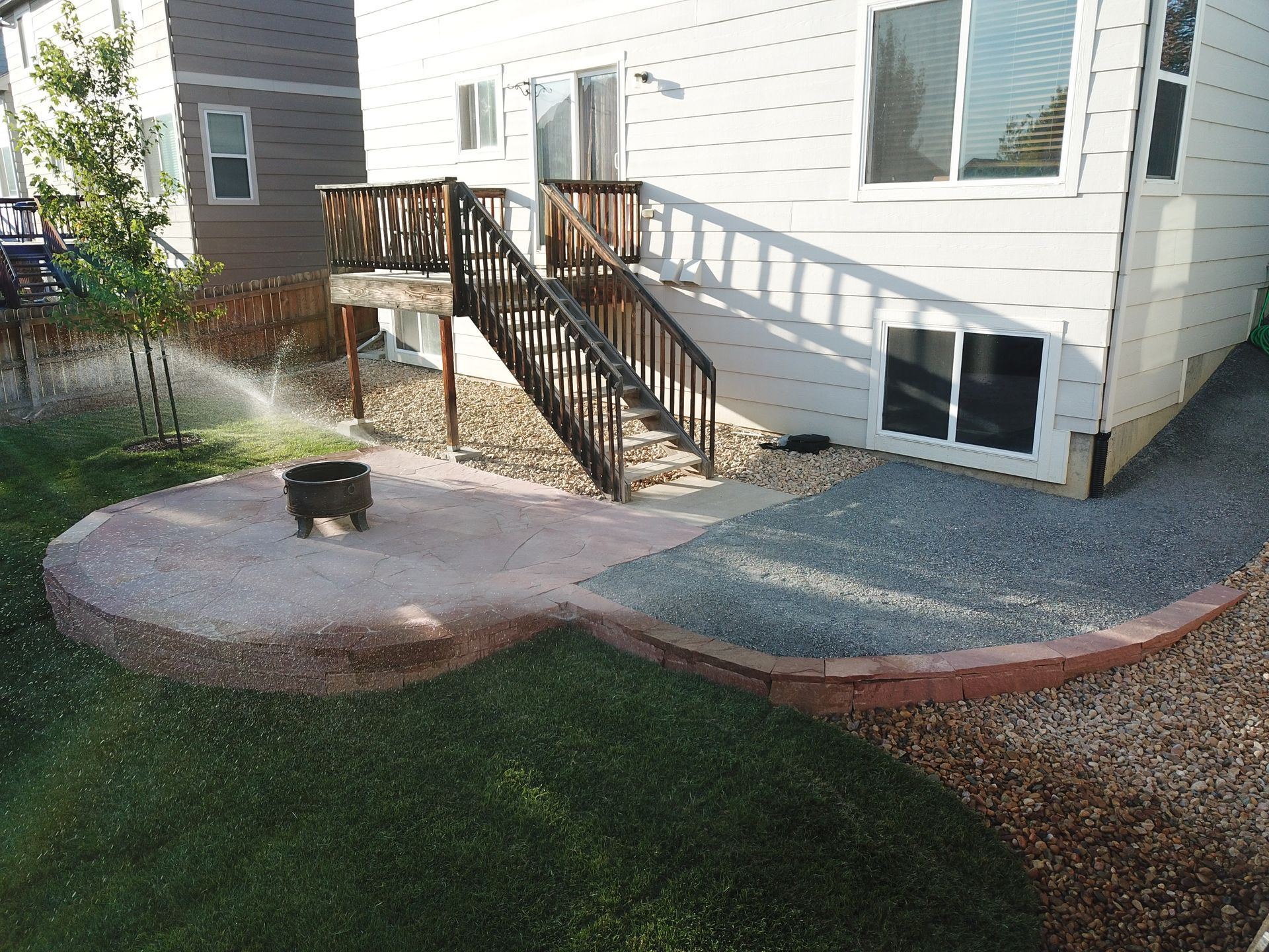 Backyard with a concrete patio, wooden stairs to a deck, and a sprinkler system.