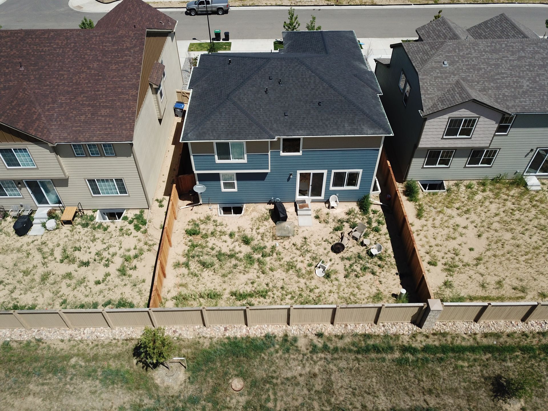 Overhead view of a blue two-story house with a small backyard between two neighboring houses.
