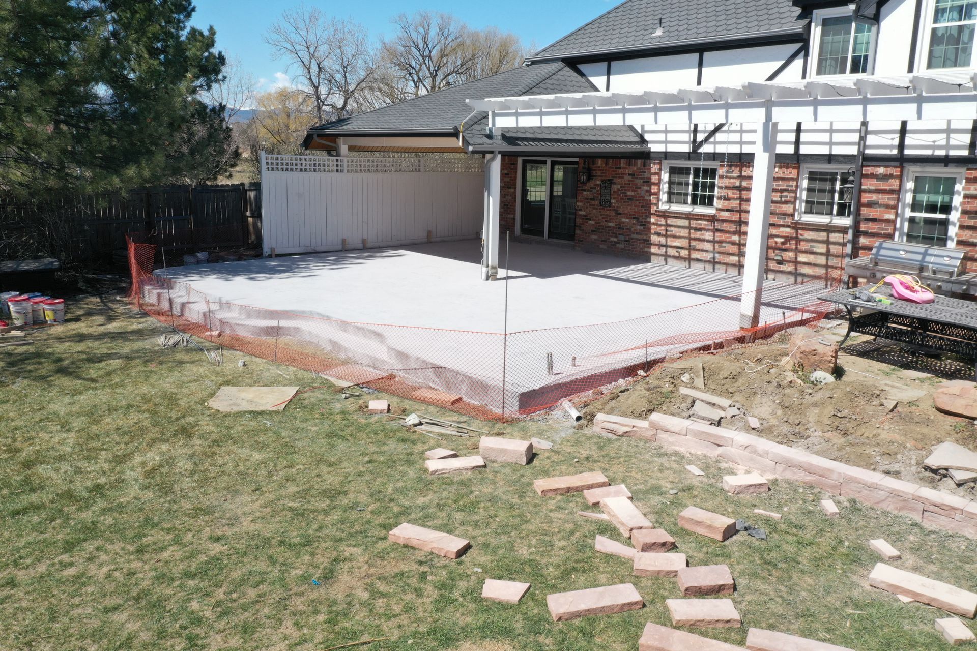 Construction of a concrete patio in a backyard with a house, pergola, and bricks.