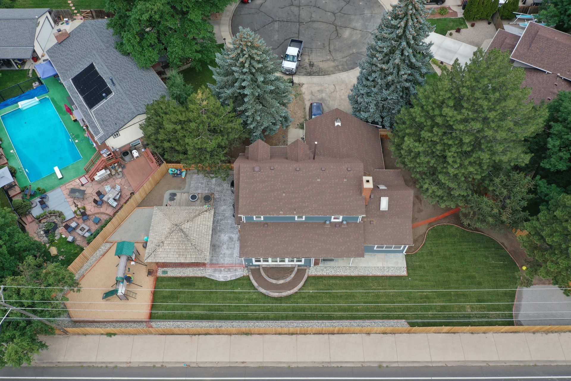 Aerial view of a house with a pool, patio, and lush landscaping on a sunny day.
