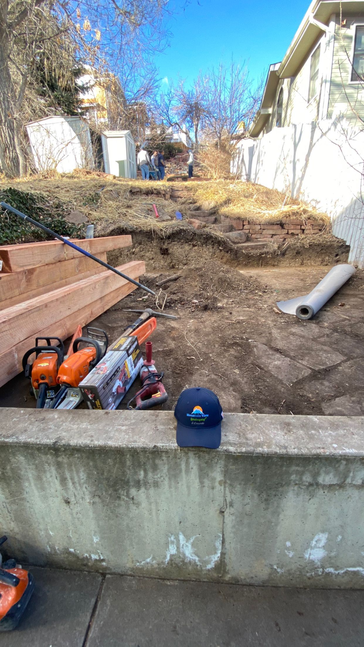 Construction site with a concrete wall, tools, and a hilly, dirt area. A cap rests on the wall.
