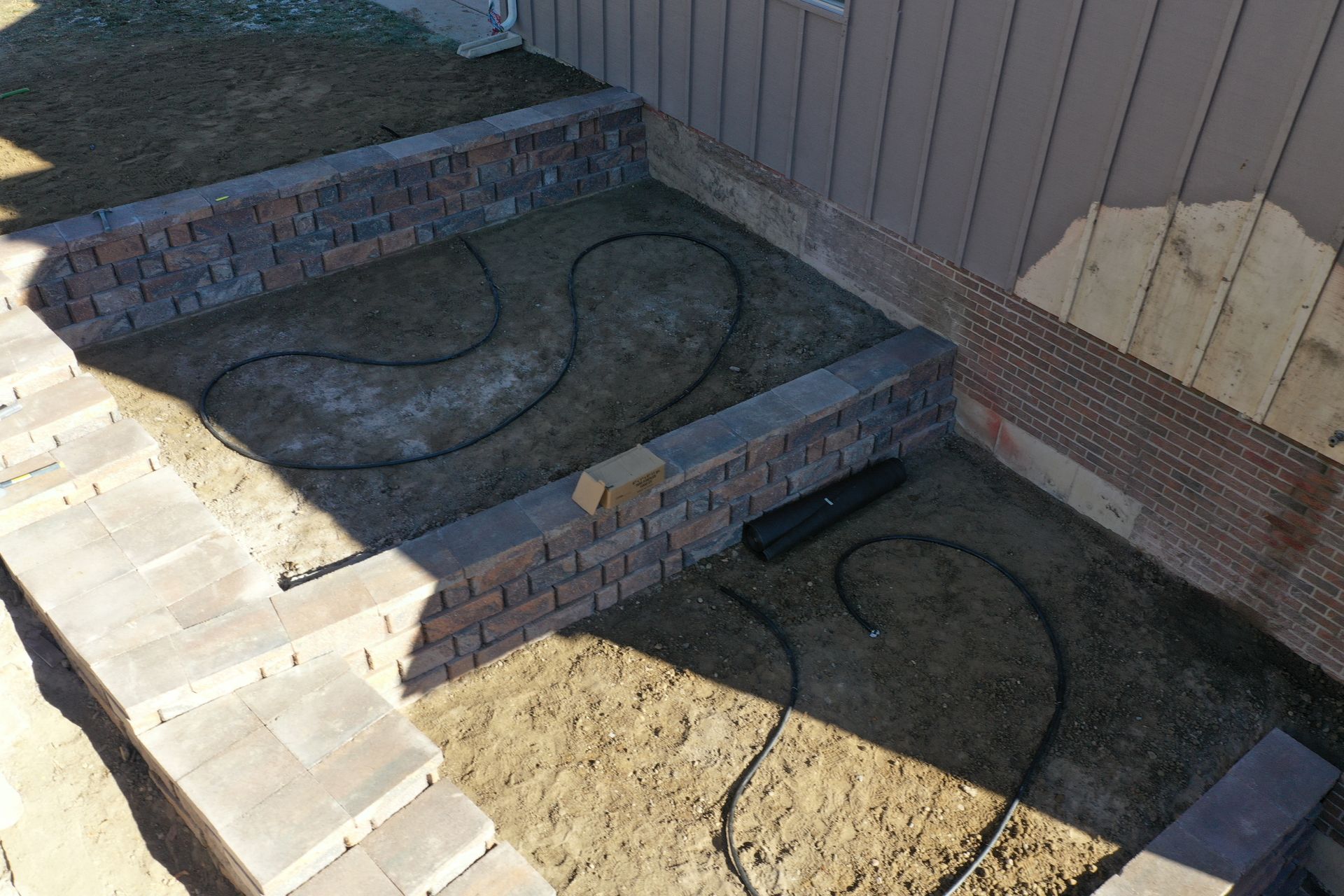 Retaining walls enclose a garden bed with irrigation lines. Brown bricks and soil are visible.