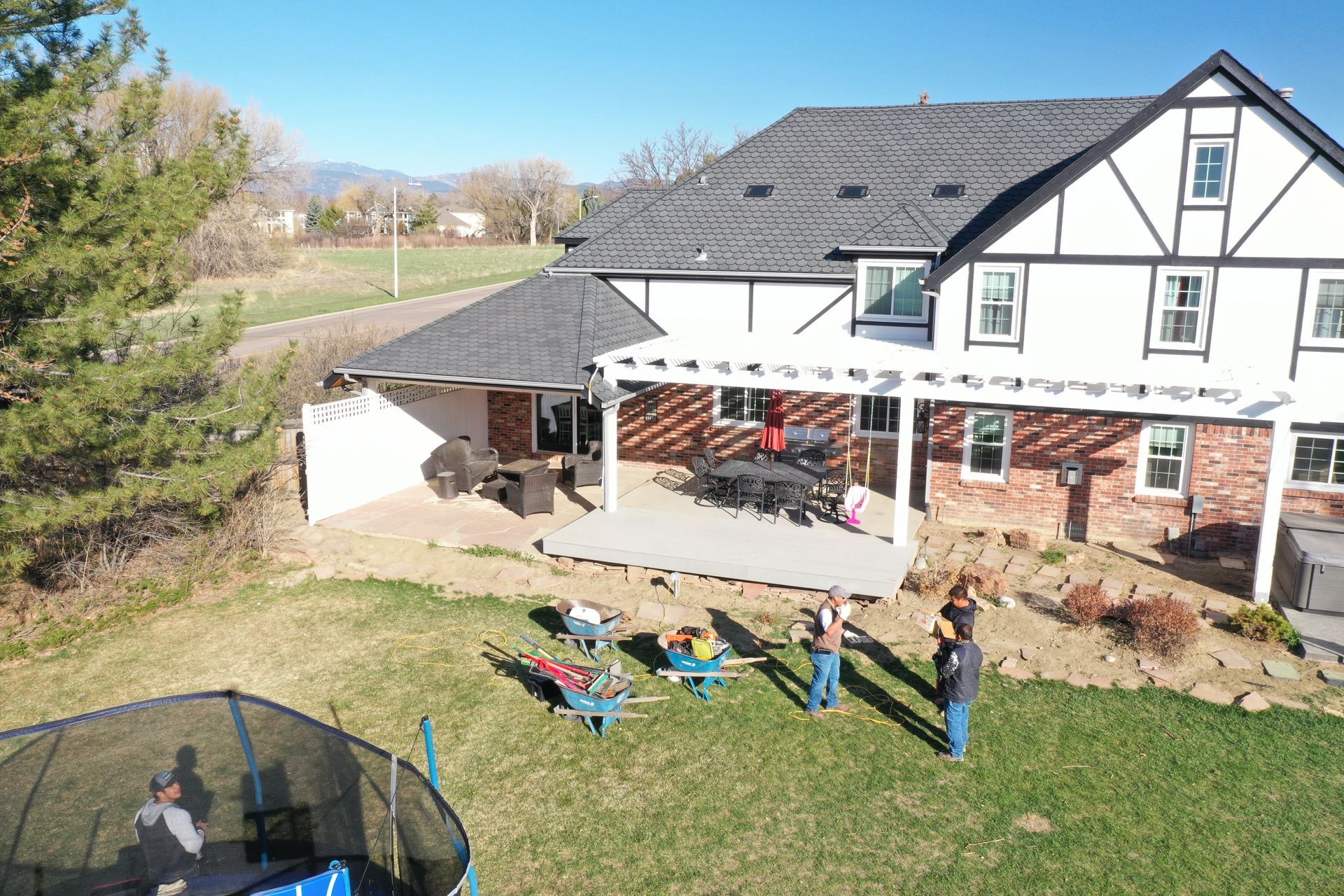 Backyard scene with a house and people near a trampoline. Sunny day.