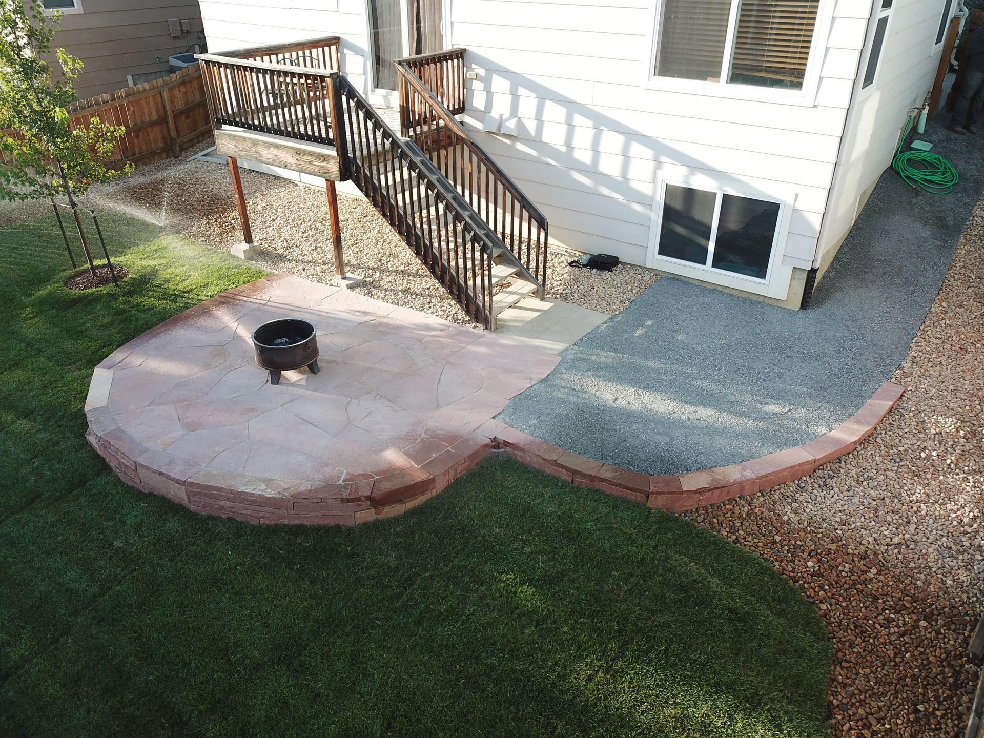 Backyard patio with fire pit, stairs leading to deck, and grass.