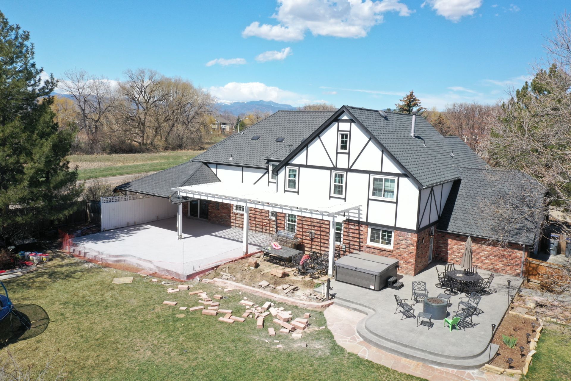 Tudor-style house with brick, white trim, and a patio area. Green lawn, blue sky, and mountain backdrop.
