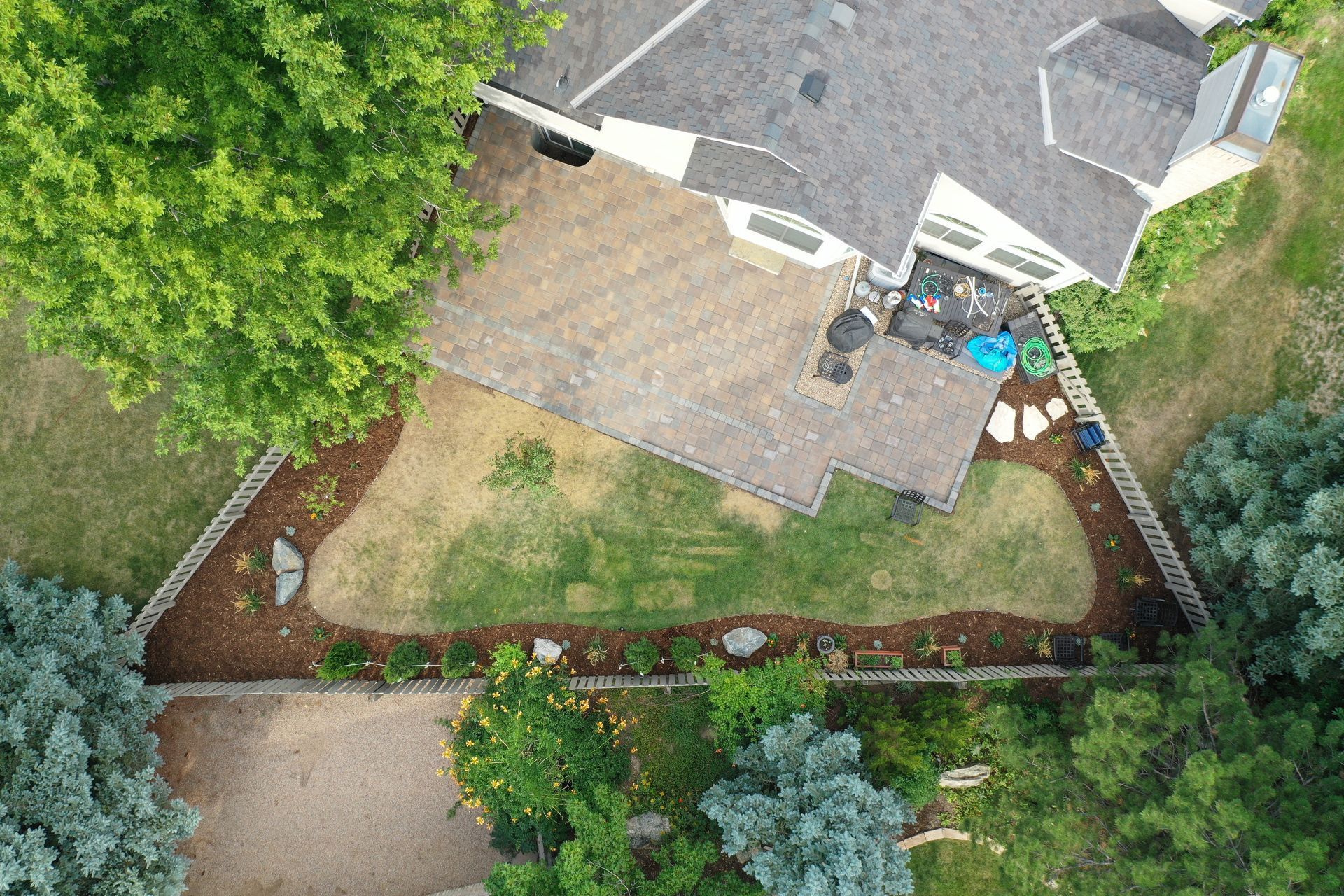 Overhead view of a house with a stone patio, lawn, garden beds, and surrounding trees.