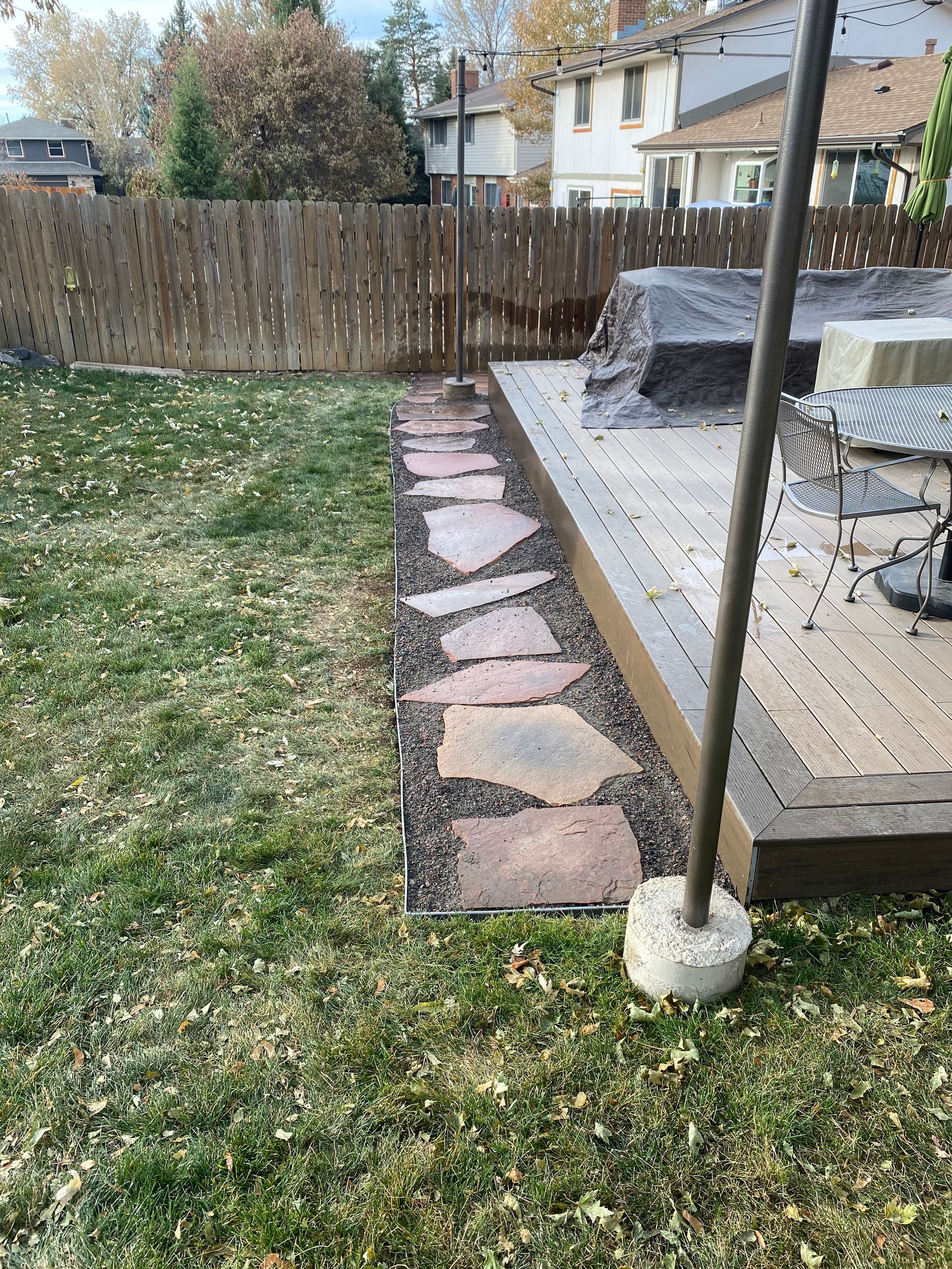 Stone pathway next to a wooden deck and a grassy yard with a wooden fence.