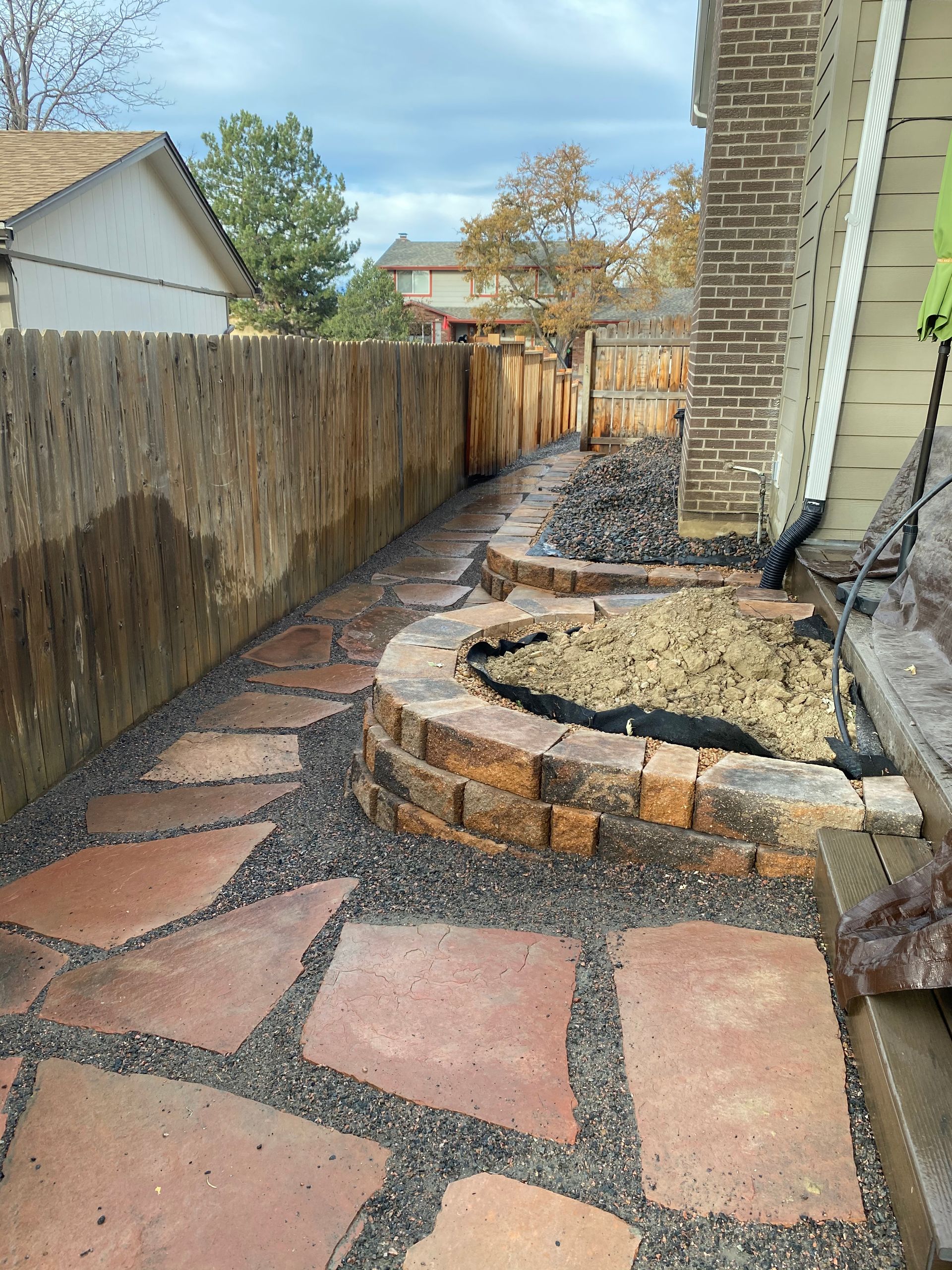 Red flagstone pathway with a retaining wall and wooden fence.