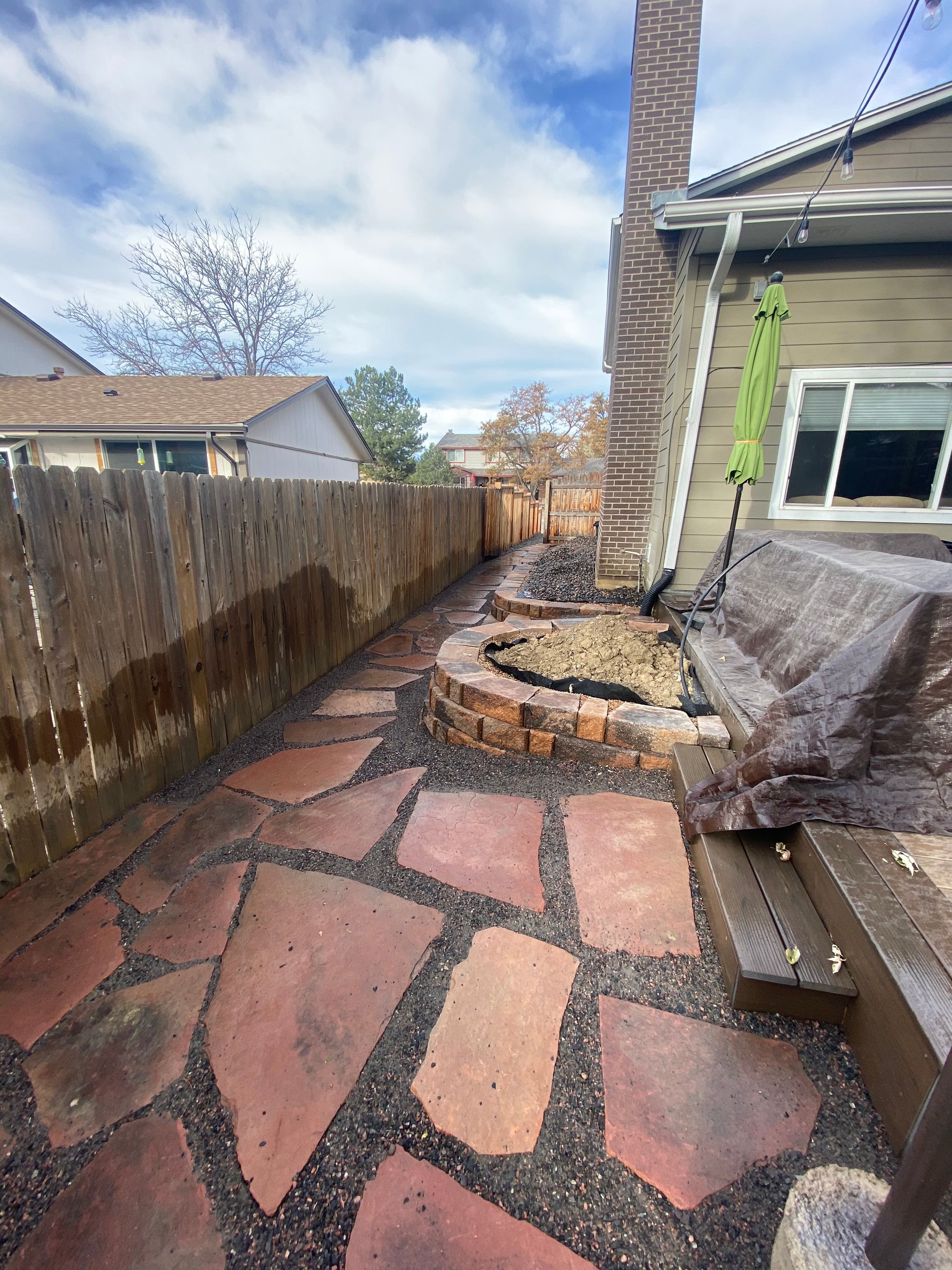Stone pathway leading to a fire pit in a backyard, with a wooden fence and house.