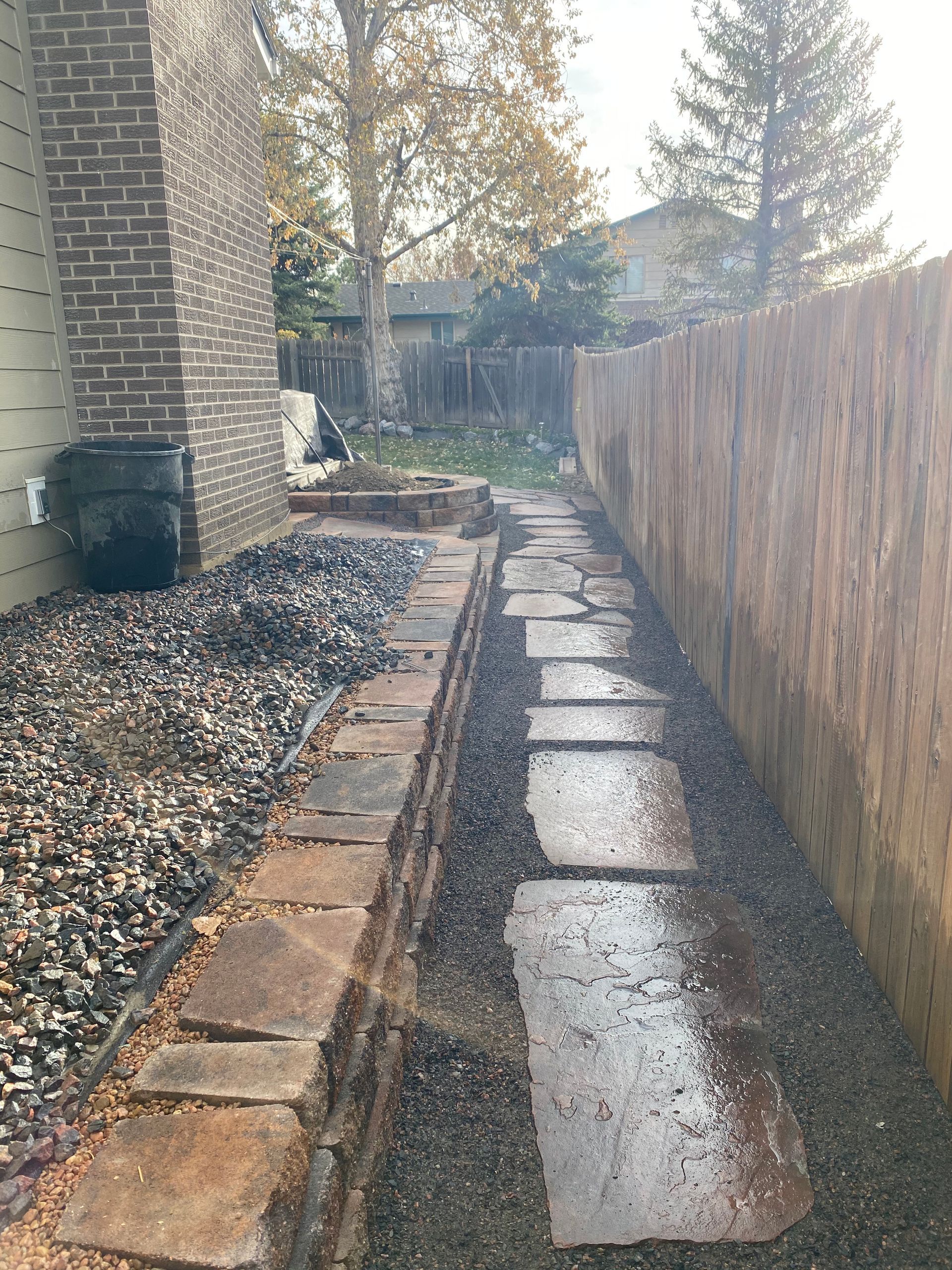 Brick path leads through a narrow backyard, bordered by a wooden fence and a stone wall.