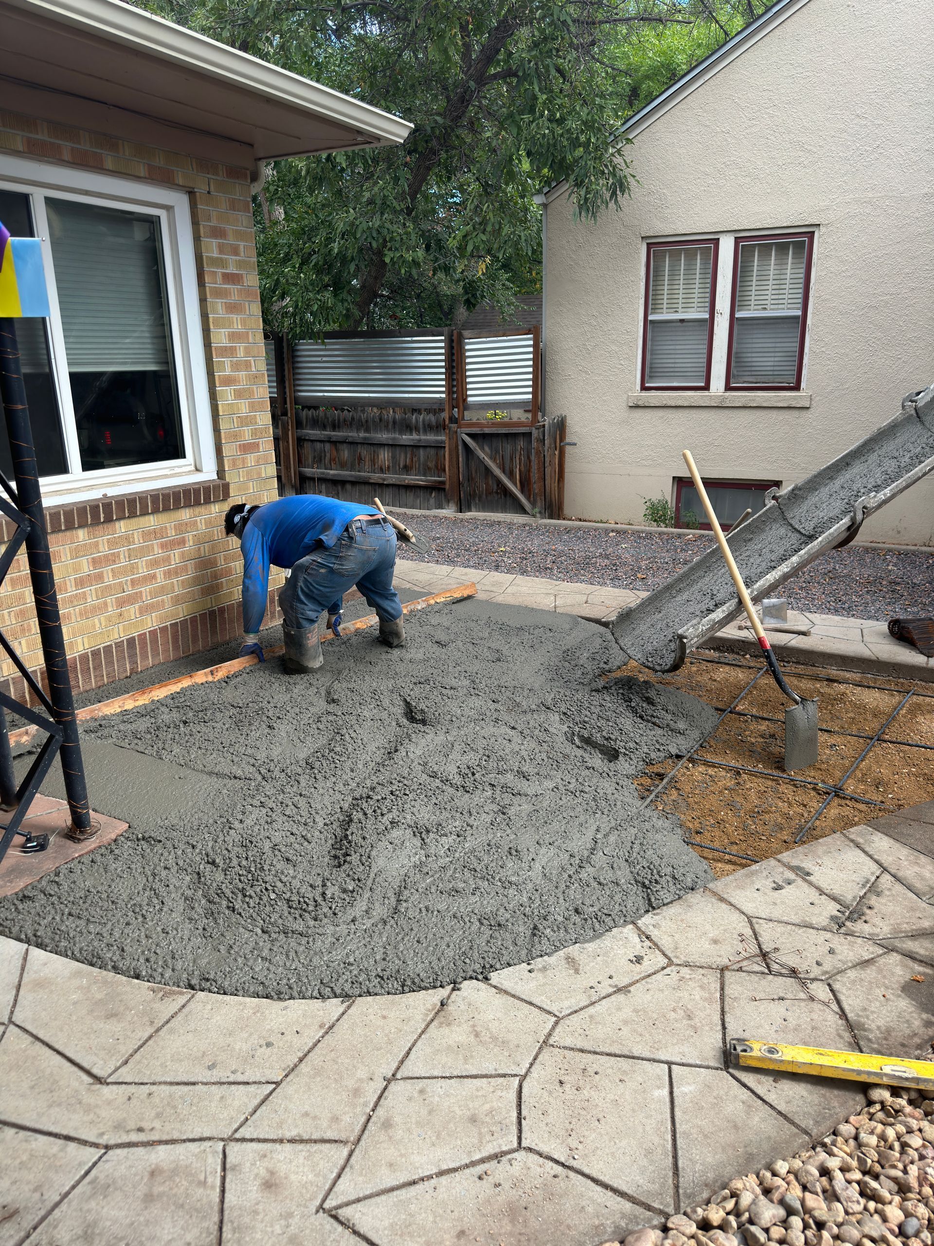 Person pouring concrete next to a house with an existing stone patio.