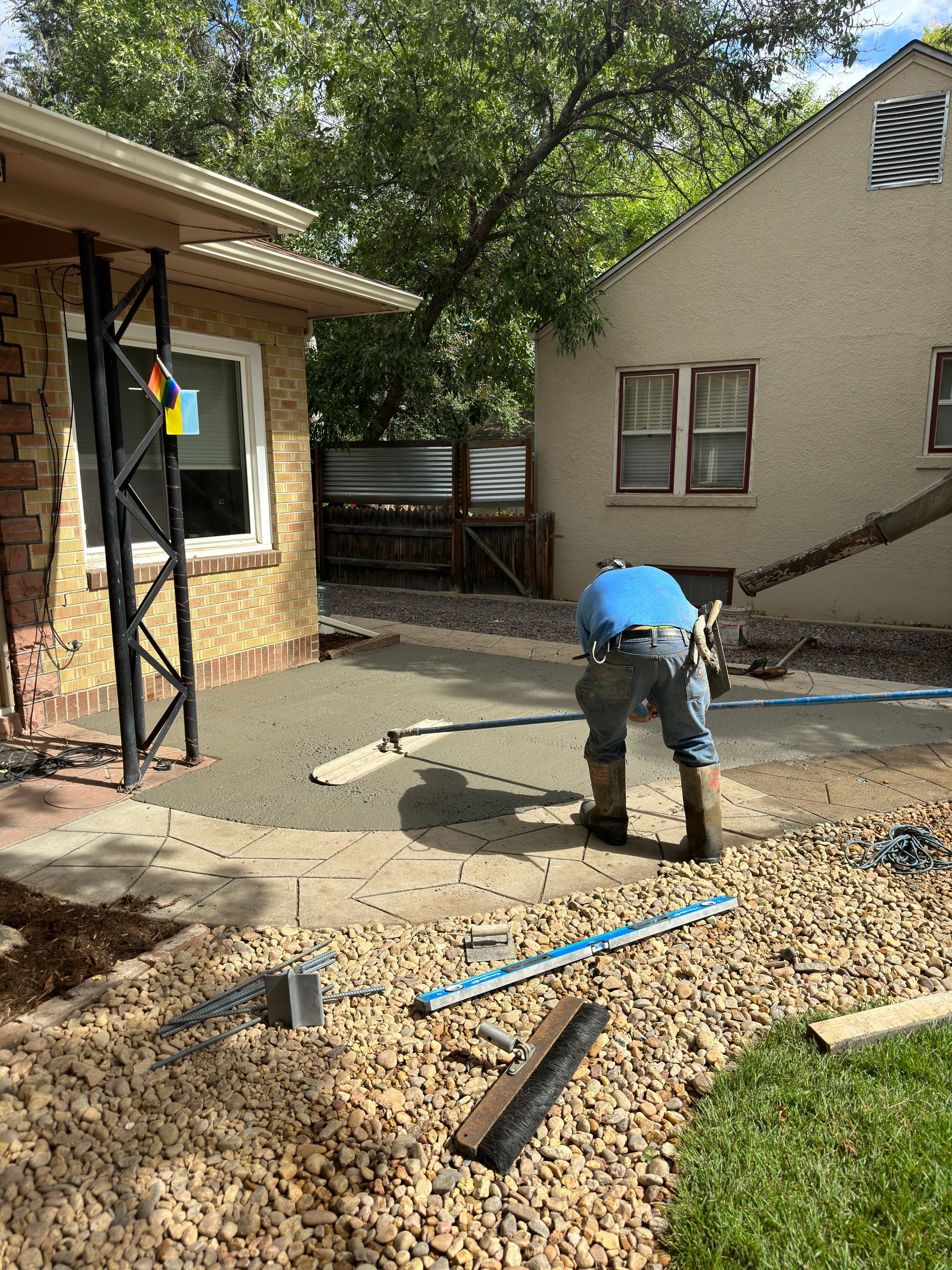 Construction worker smoothing wet concrete on a patio. House and trees in the background.