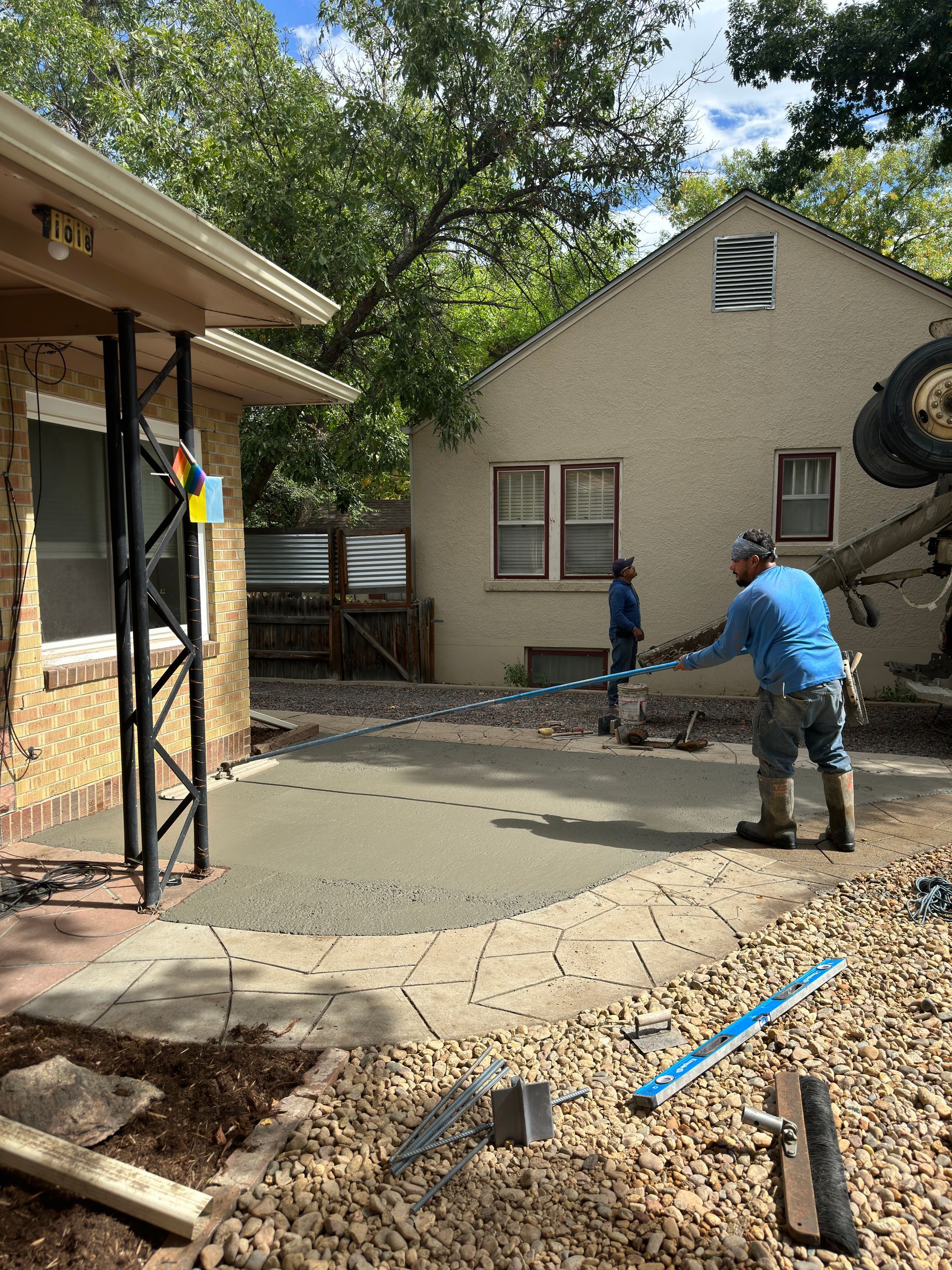 Construction workers pouring concrete for a patio. A house and yard are in the background.
