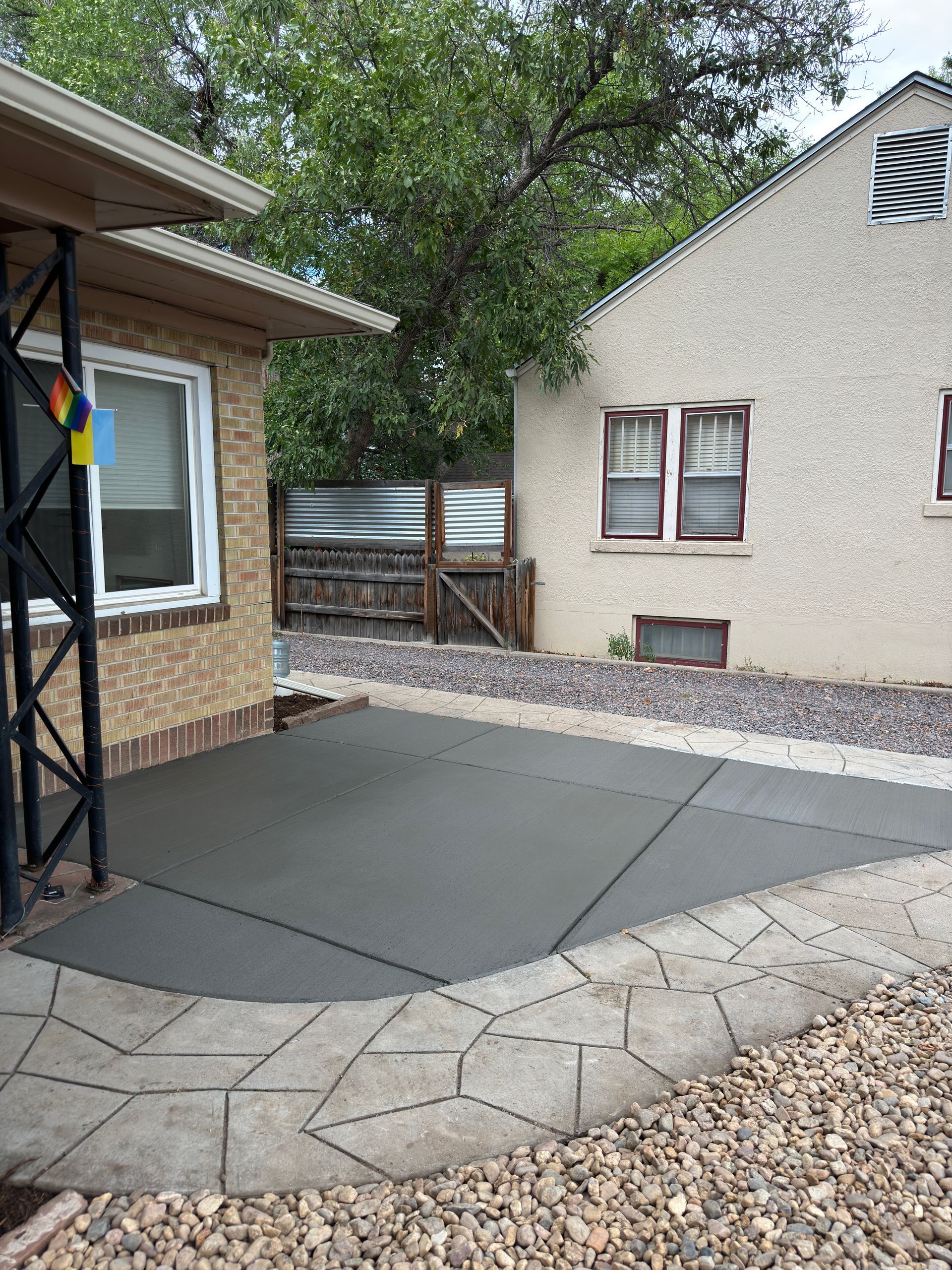 A concrete patio with a decorative border next to a brick house and gravel.